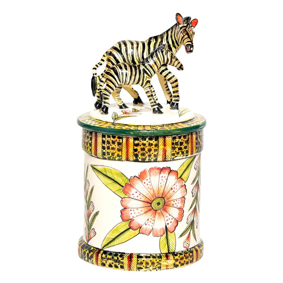 Wiseman Ceramics introduces a ceramic Zebra on Daisies cookie jar, crafted by artisans Riya and George-Thabo in South Africa. Standing 9 inches tall with dimensions of 6 inches in length and width, this piece features a hand-painted zebra and baby