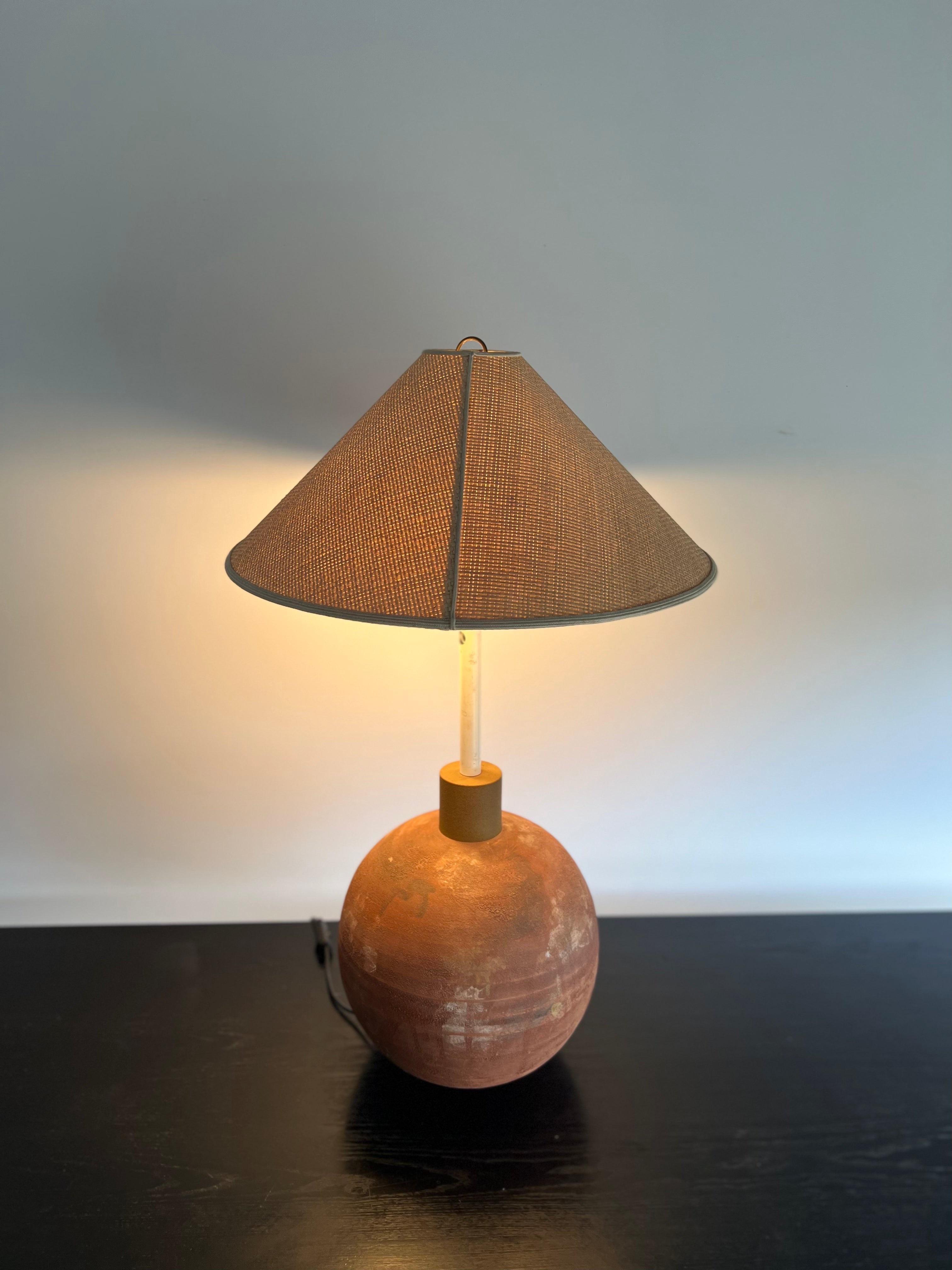 La lampe est dotée d'un abat-jour sphérique en terre cuite dans un ton chaud et terreux, complété par une base chromée élégante. L'abat-jour est conçu avec de petites perforations qui créent un magnifique motif lumineux lorsque la lampe est allumée.