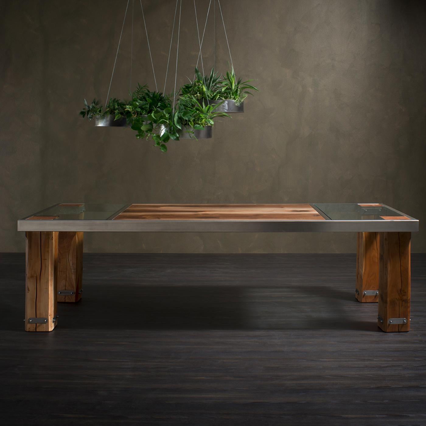 An example of refined craftsmanship, this splendid table combines an intense, naturally colored cherry structure with a solid satin steel frame. The robust legs function as both structural and decorative elements, together with the carved cherry