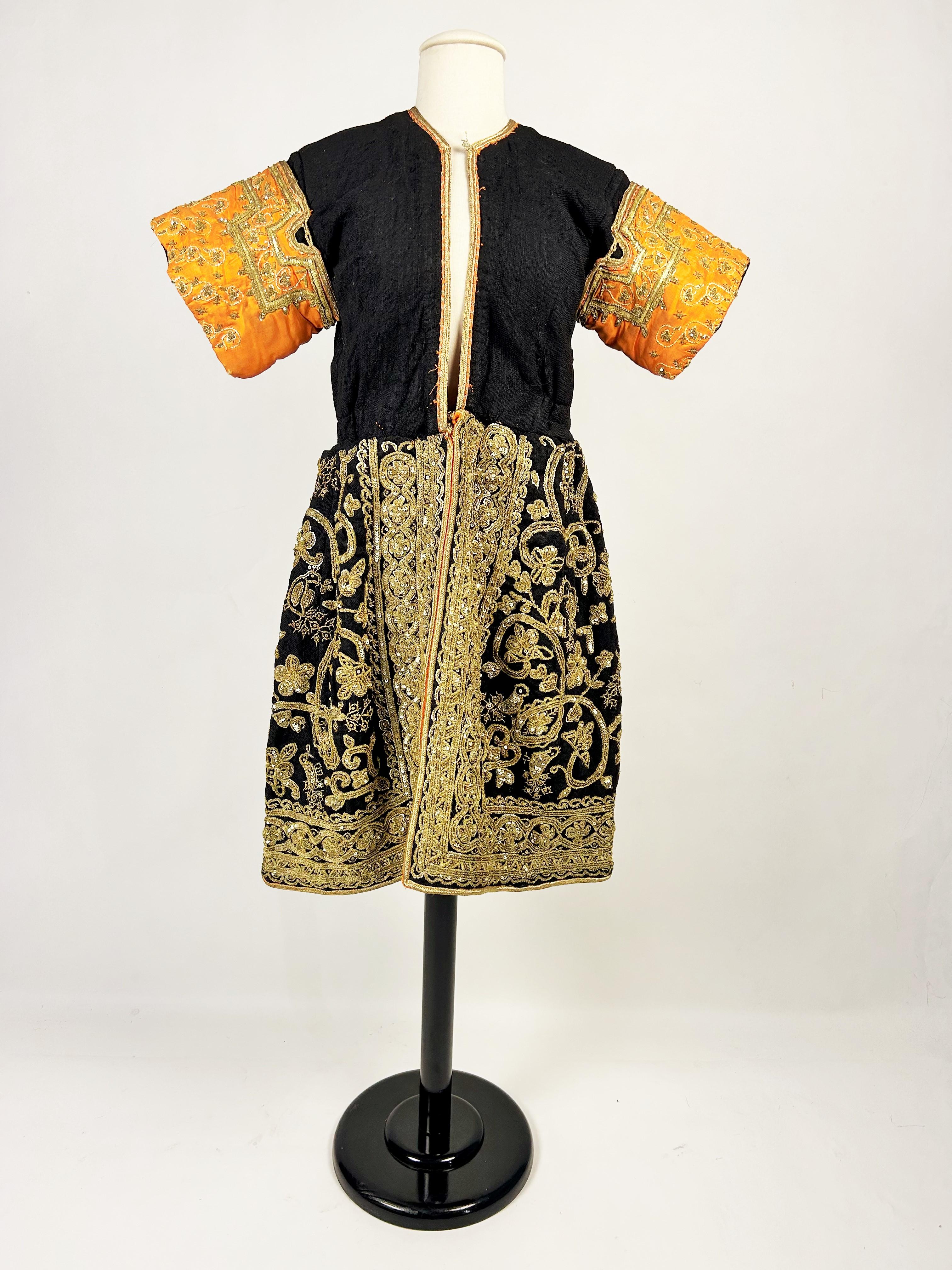 Vers 1940-1960
Tunisie Hammamet
Spectaculaire robe de mariée tunisienne de la région de Hammamet, datant du milieu du XXe siècle. Coupe droite, légèrement bouffante sur les hanches, ouverte sur le devant. Tissu de laine noire densément brodé de