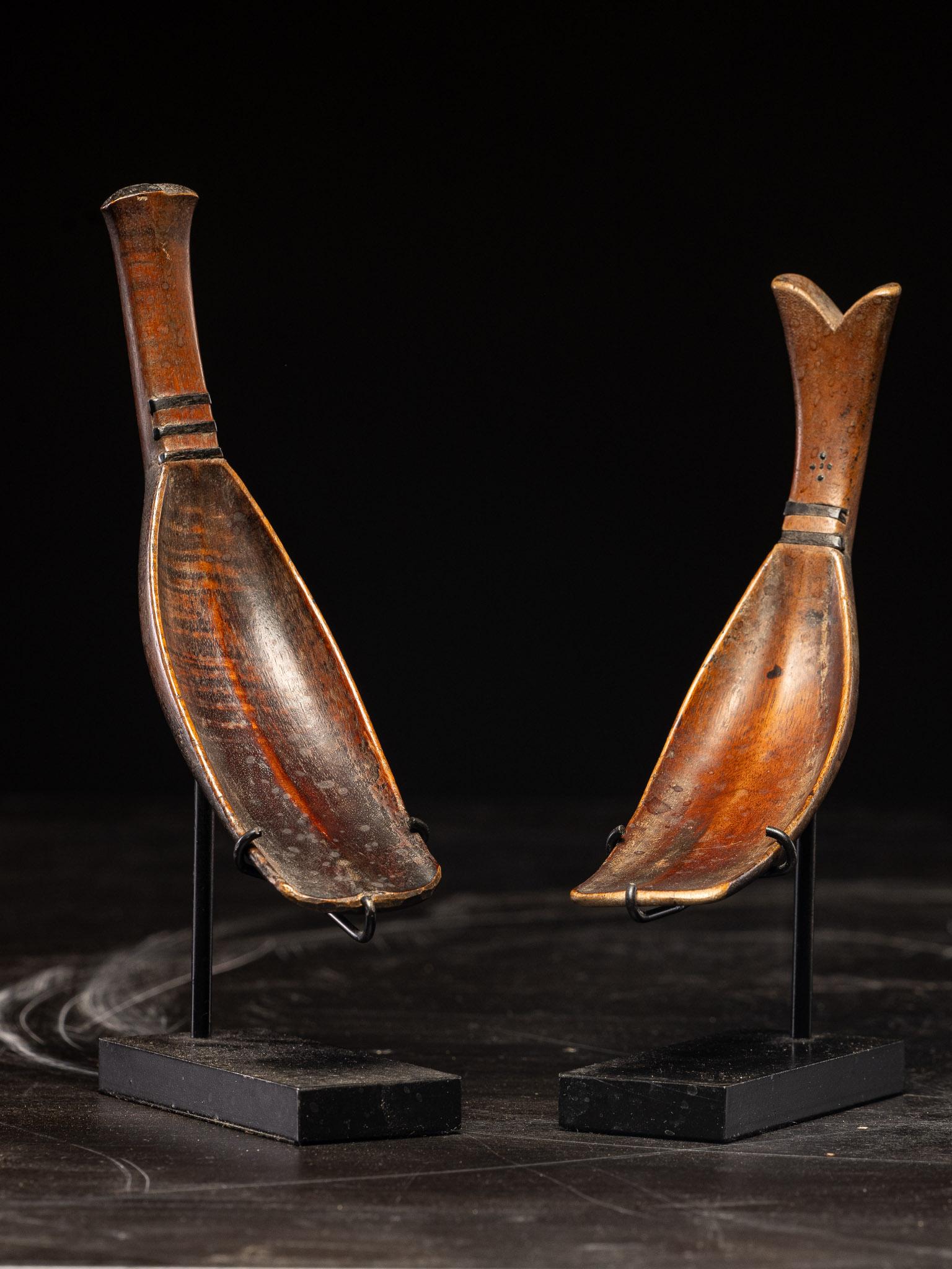 A pair of exquisite Toraja rice spoons from Indonesia's Sulawesi Islands, featuring elongated bowls and gracefully curved handles that complement the overall design. Each spoon is intricately carved with delicate, elegant lines, showcasing a rich