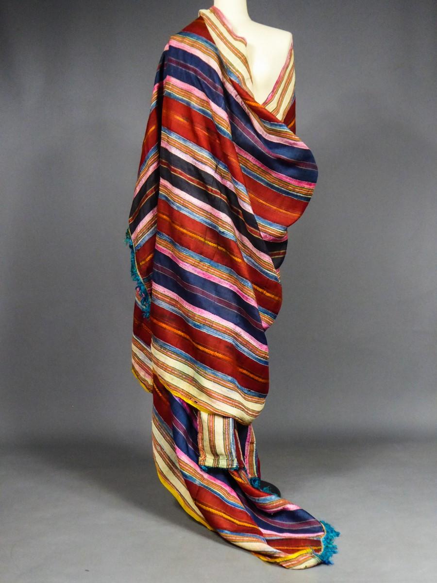 Circa 1900/1950
Tunisia

Very long ceremonial shawl in strips of sewn silks originally from Tunisia and dating from the first half of the 20th century. Large shaped silk bands alternating with narrower stripes with very strong polychromy and tapered
