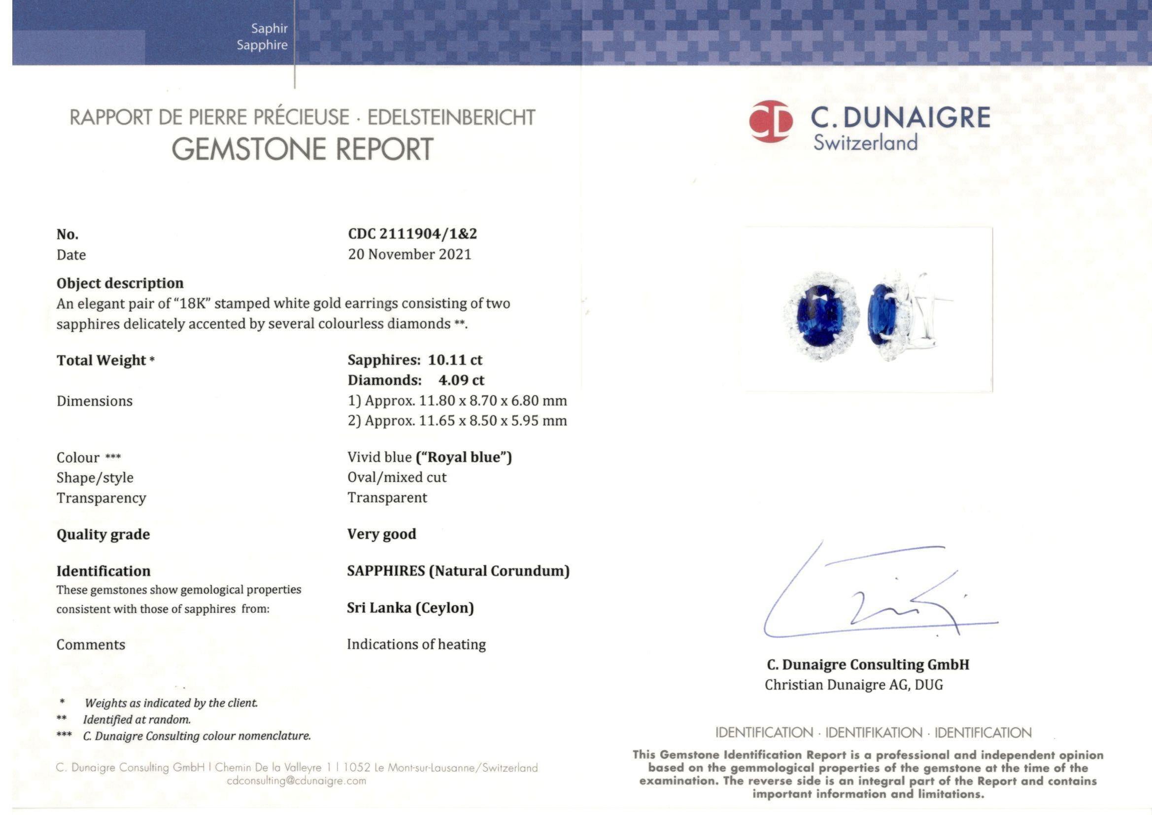 Showcasing two color-rich Certified oval cut Blue Sapphire weighing 10.11 carats total, surrounded by a single row of oval cut brilliant diamonds. 16 Accent diamonds weigh 4.09 carats total. Set in 18 karats white gold. Omega Clip with the