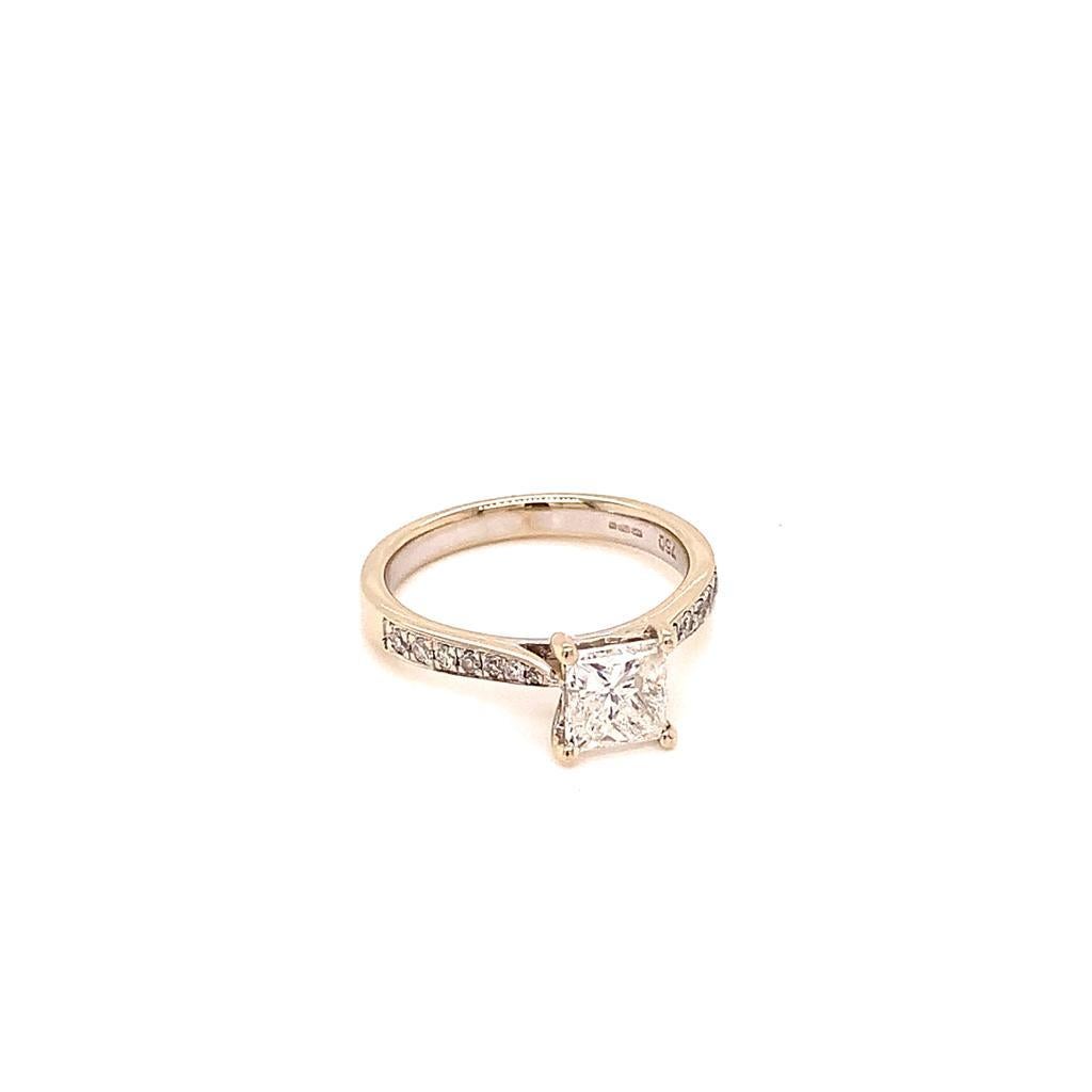 This elegantly radiant ring features an alluring 1.12 Carat Princess cut Diamond of F colour and SI2 clarity at its centre, making it flawless to the naked eye. This impeccable diamond is surrounded by 14 scintillating side diamonds of F-G colour