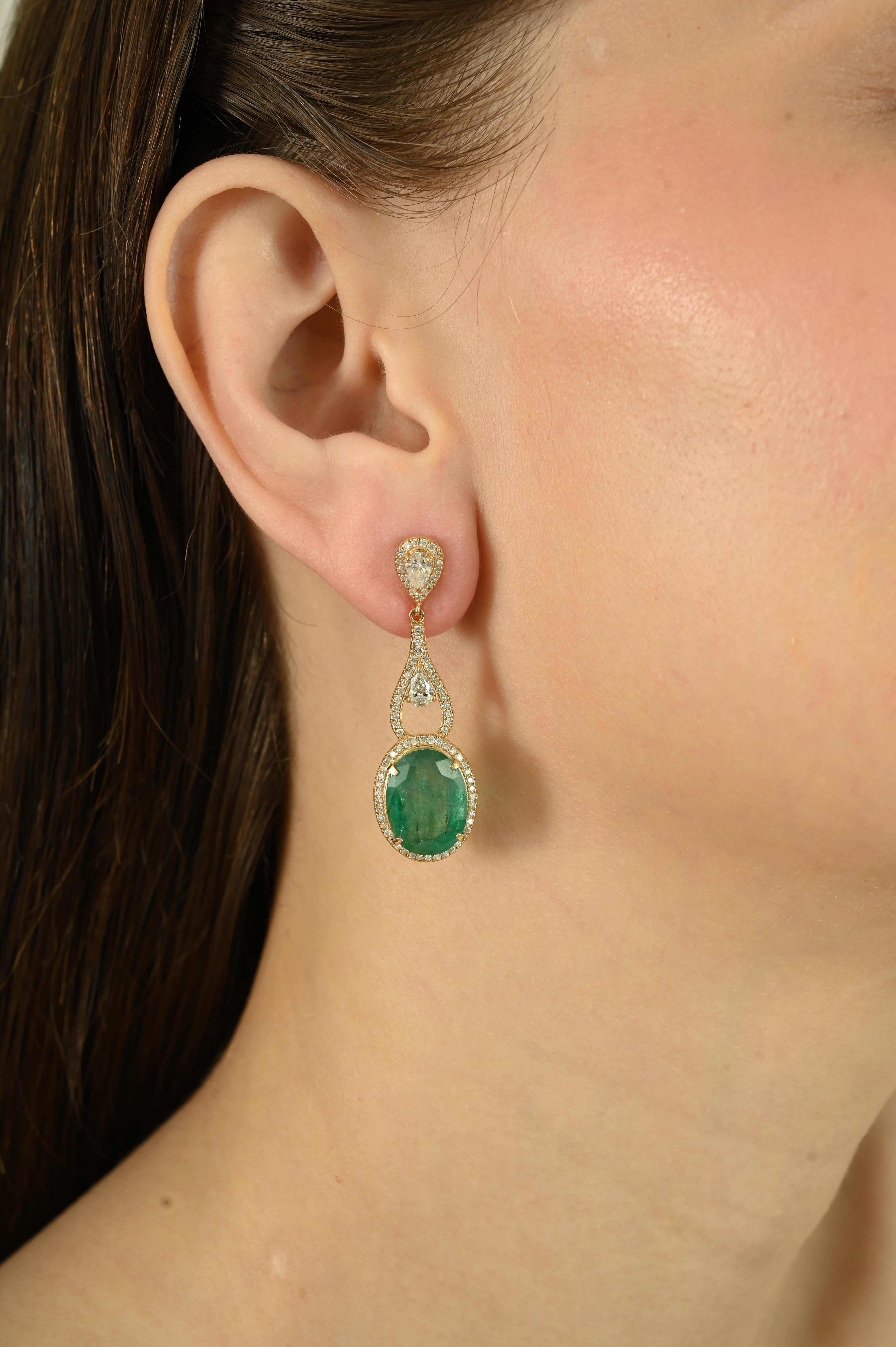 These certified 14.04 carat Zambian emerald dangle earrings feature two stunning oval-cut emeralds totaling 14.04 carats, beautifully accented by round brilliant-cut diamonds with a total weight of 1.78 carats. Expertly handcrafted in 18k yellow