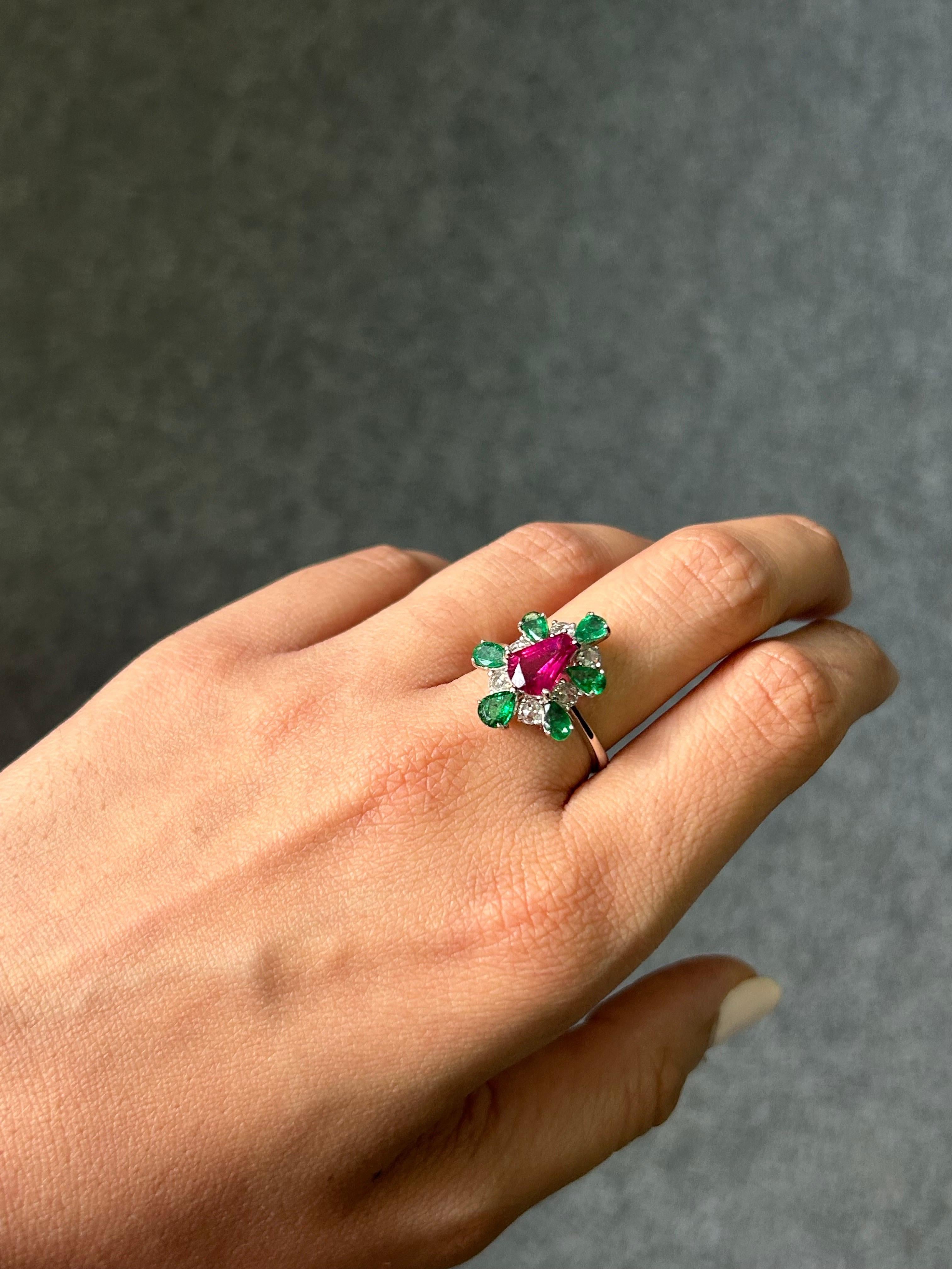 One of a kind, fancy shaped certified no heat Mozambique Ruby ring, adorned with pear shape Zambian Emeralds and rose-cut Diamonds, set in 18K White Gold. The beautiful pink/red hue of the Ruby complements the vivid green of the Emeralds, making it