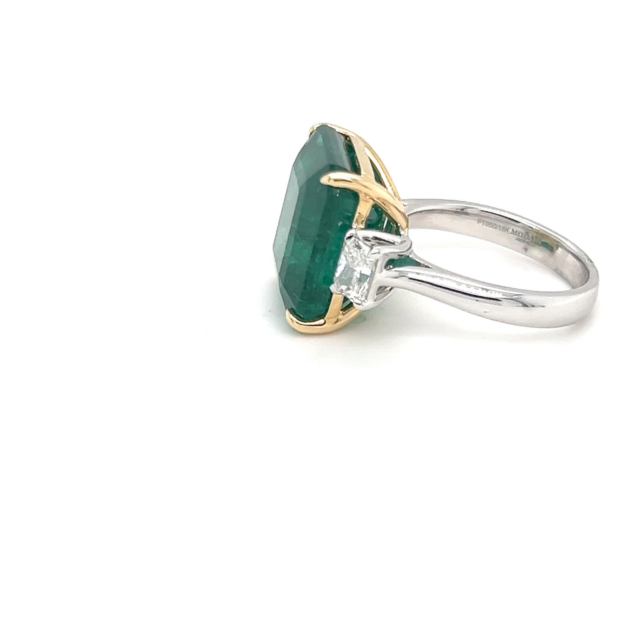 This breathtaking 15.01-carat octagon-cut emerald ring features a striking center stone, accented by two radiant-cut diamonds weighing a total of 1.03 carats, set east to west. The vibrant emerald is held securely in yellow gold claws, while the