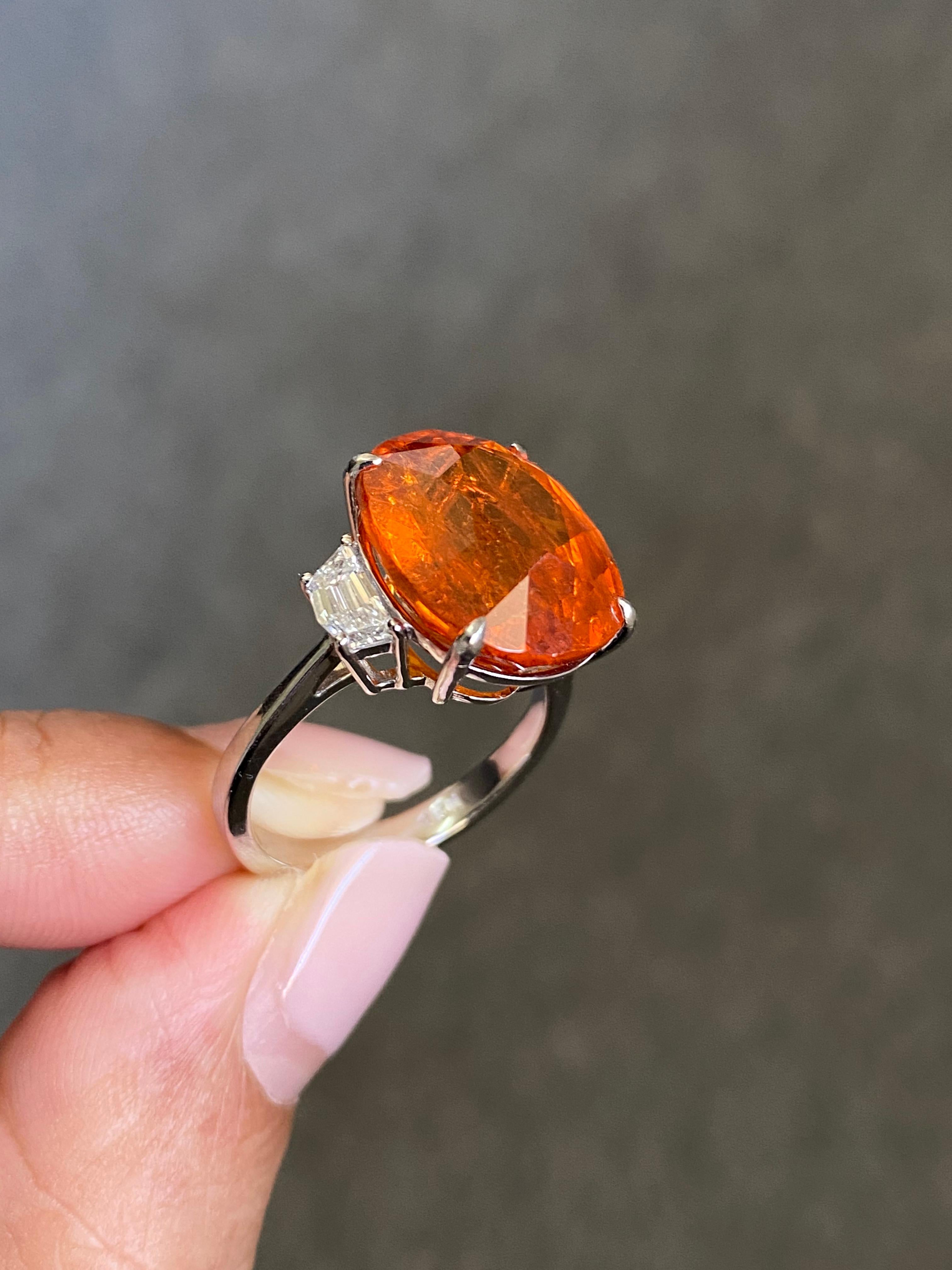 Ein atemberaubender Verlobungsring mit drei Steinen, mit einem 15,48 Karat transparenten, ovalen, natürlichen Mandarin-Granat als Mittelstein und 0,65 Karat Diamanten in Cadillac-Form als Seitenstein in VS2-Qualität. Der Mandarin-Granat ist von
