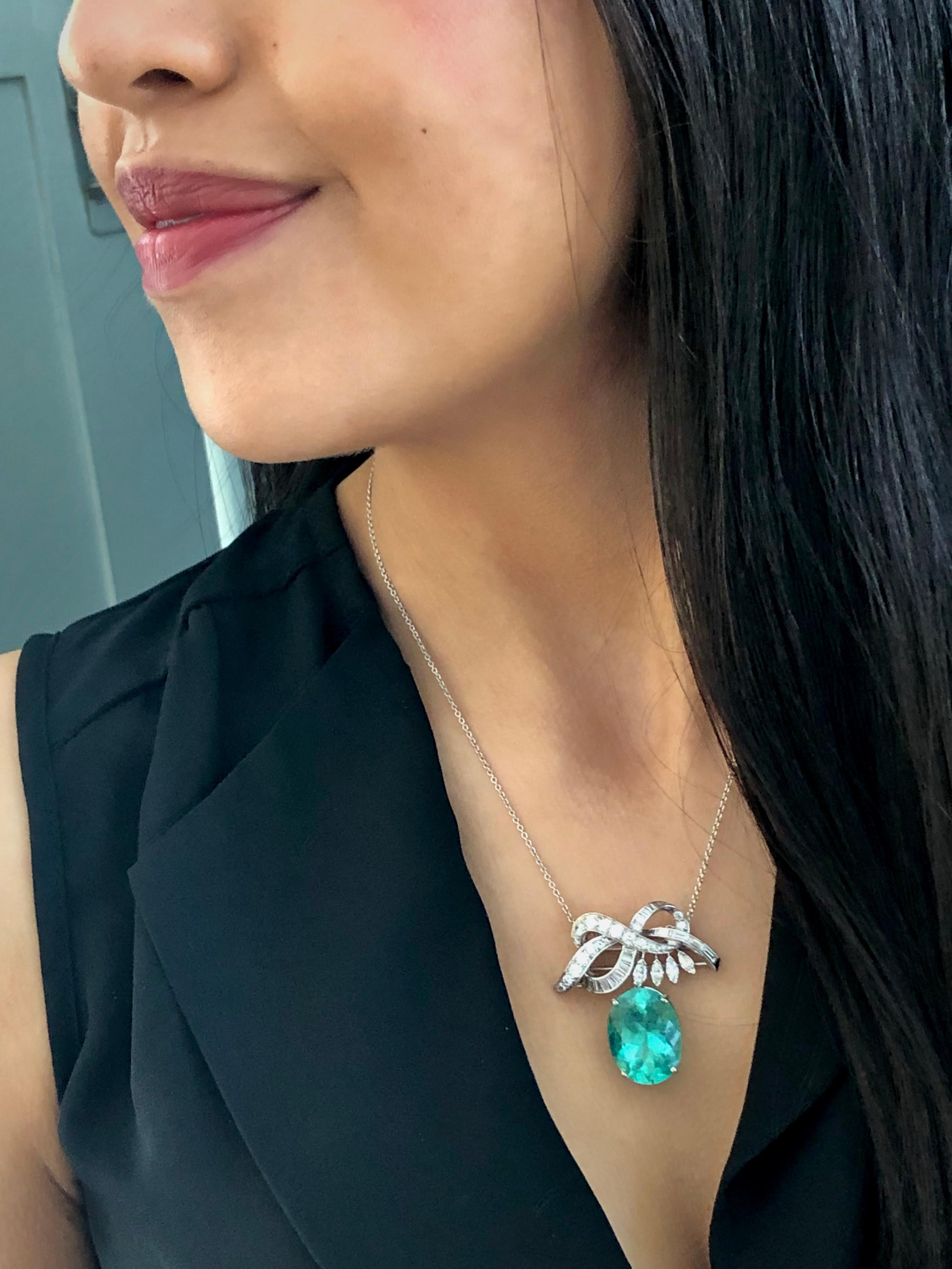An exquisite statement Brooch/Pendant necklace featuring an oval cut natural Colombian emerald weighing 16.16 carats set in a ribbon motif brooch. The ribbon is set with tapered baguette, step-cut diamonds, marquise-cut diamonds, and graduated