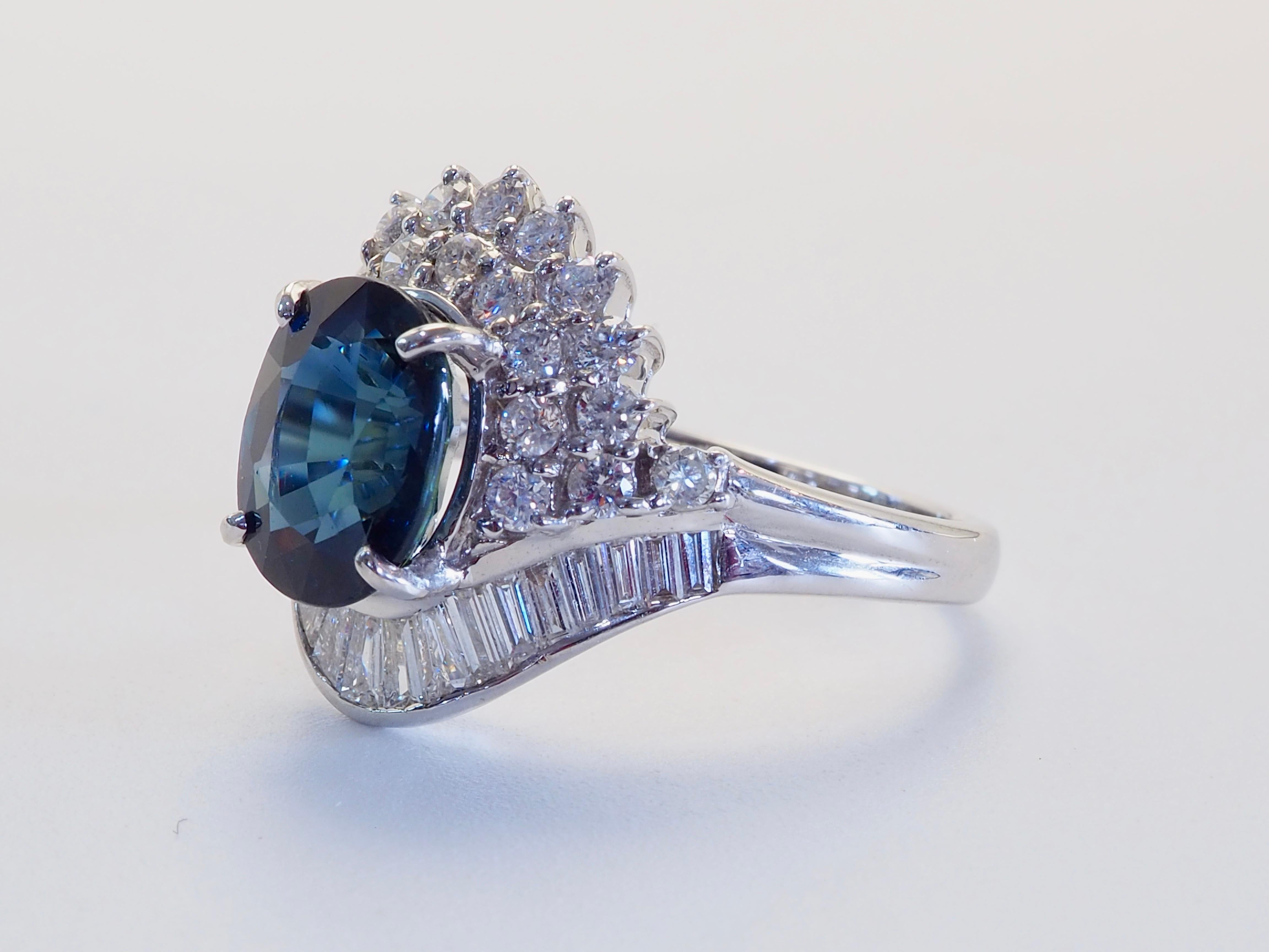 Incredibile anello che vanta uno zaffiro tailandese di straordinaria bellezza. Lo zaffiro ovale tailandese è di dimensioni discrete e presenta un'impressionante tonalità scura di colore blu verdastro. Brillanti e diamanti a baguette di alta qualità