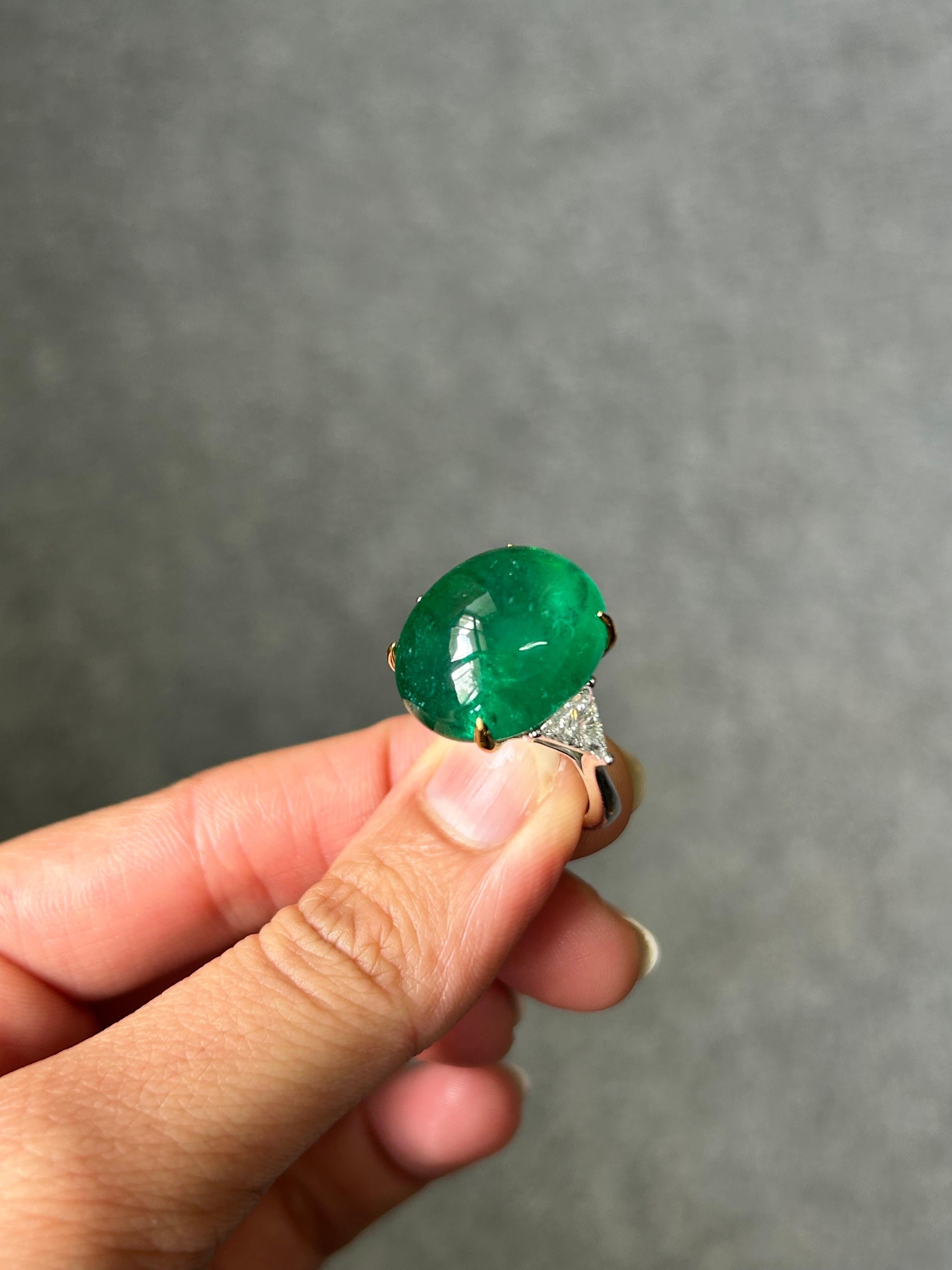A stunning certified 20.47 carat, Zambian Emerald Cabochon center stone  with 0.71 carat VS quality trillion side stones, set in 18K White Gold. The center stone has a beautiful luster, and vivid green color and great transparency. Currently sized