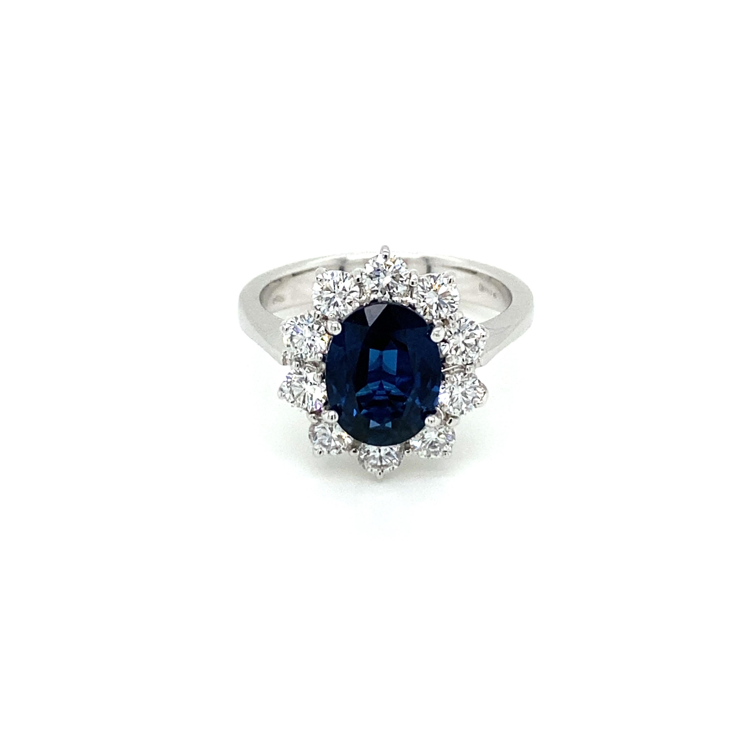 A fine and impressive 18k white Gold, Blue Sapphire and Diamond cluster Ring, set in the center with an oval-cut Natural Burma Sapphire weighing 2.10 carats. The gemstone features vivid color saturation and medium to dark tone with extraordinary
