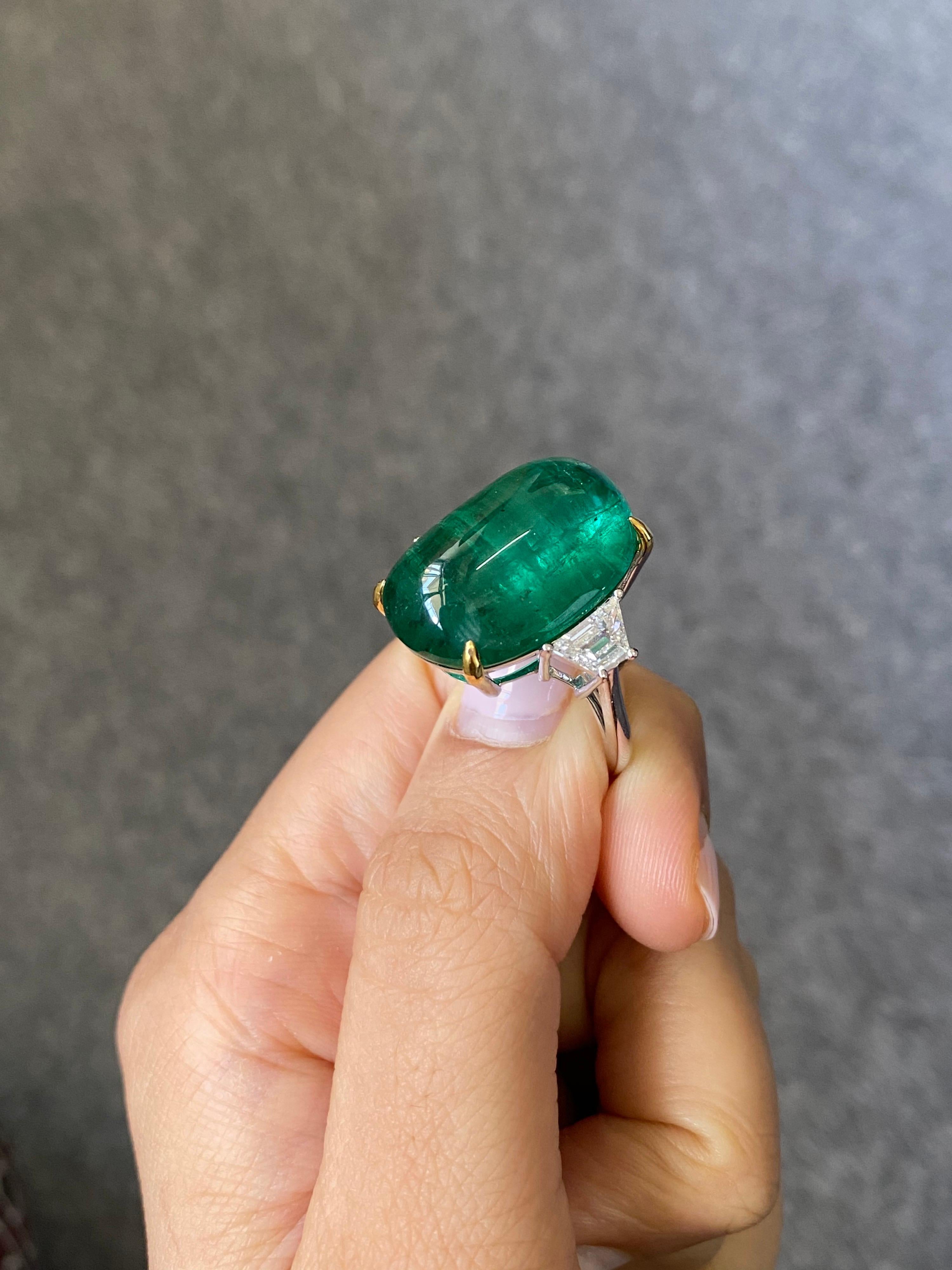 One of a kind, unisex, 23.82 carat natural Zambian Emerald cabochon three-stone engagement ring, with 0.89 carat trapeze VS quality  White Diamonds. The centre stone is transparent, with an idea vivid green color and beautiful luster. The Diamonds