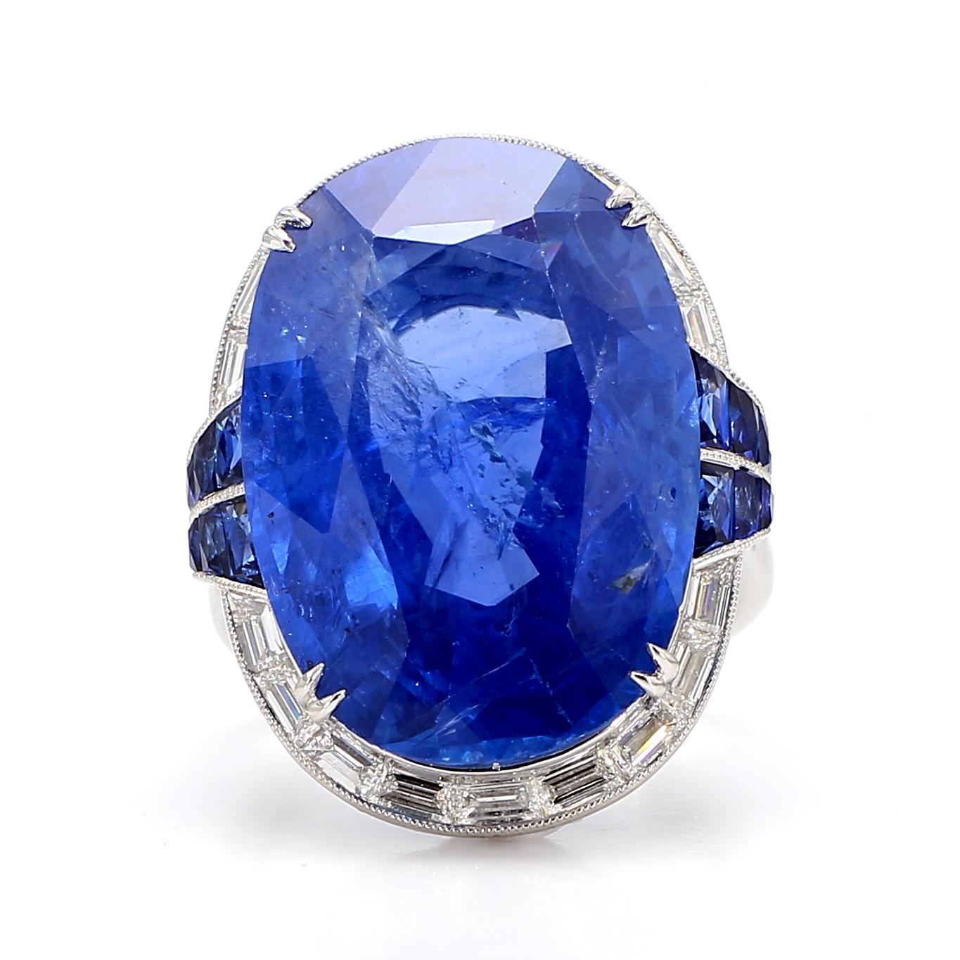 This exquisite ring showcases a magnificent 24.33 carat oval-cut sapphire, radiating a deep blue hue. The sapphire is elegantly accented by a series of white diamonds, totaling 0.78 carats. These diamonds are baguette-cut, with a clarity of VS2 and