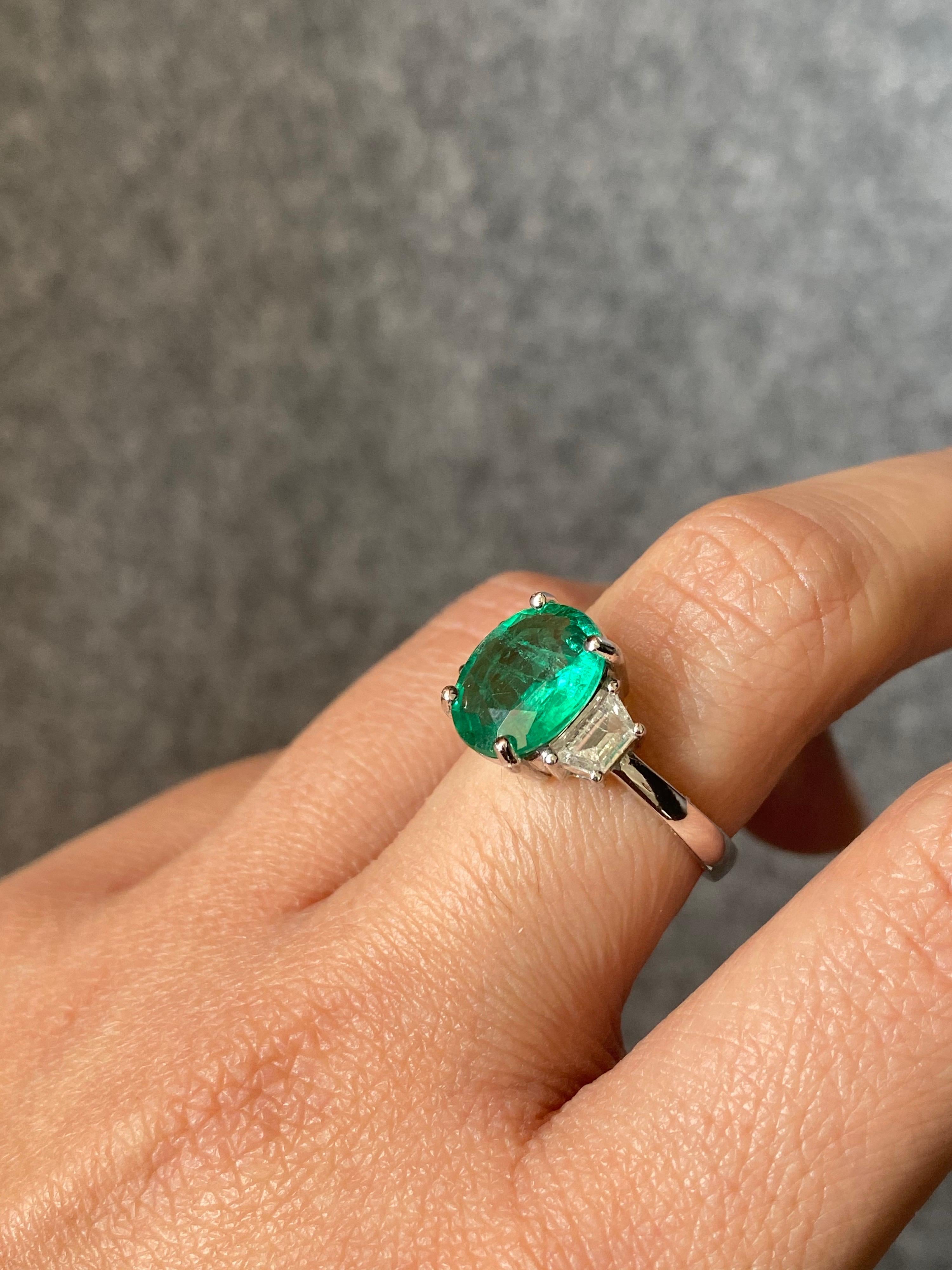 A beautiful oval-shape Zambian Emerald stone, weighing 2.56 carats - transparent with very few inclusions. It's a vivid green Emerald, which is an ideal color for the stone. The 2 trapezoid Diamonds are colorless, VS quality and weigh 0.44 carats in