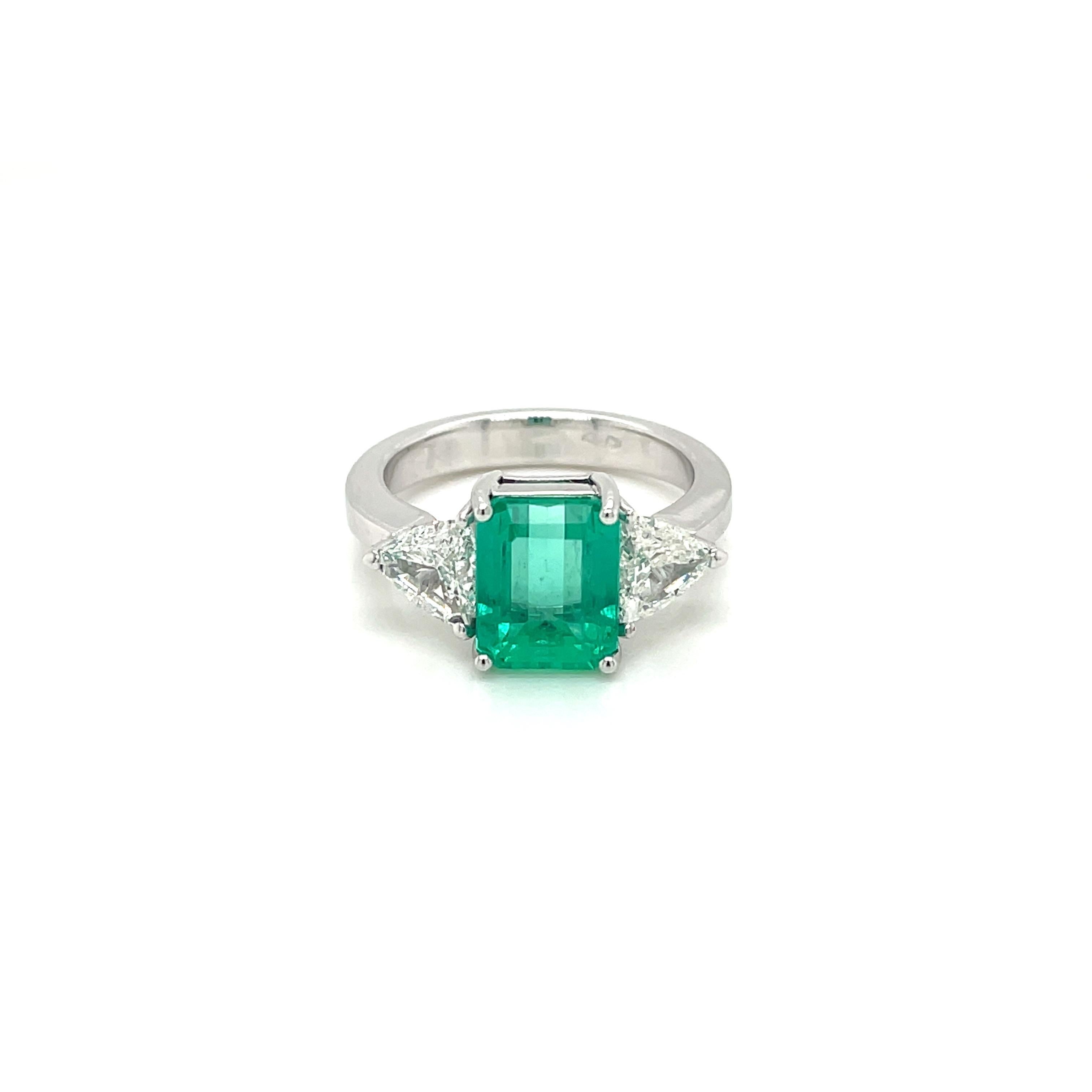 An exquisite ring set in 18k white gold, contemporary, featuring a vivid green 2.93 ct Emerald-cut Colombian Emerald, surrounded by 2 Diamonds triangle cut, 0,50 ct each for a total weight of 1 carat, graded G/H color Vvs1 , graded G color Vvs1