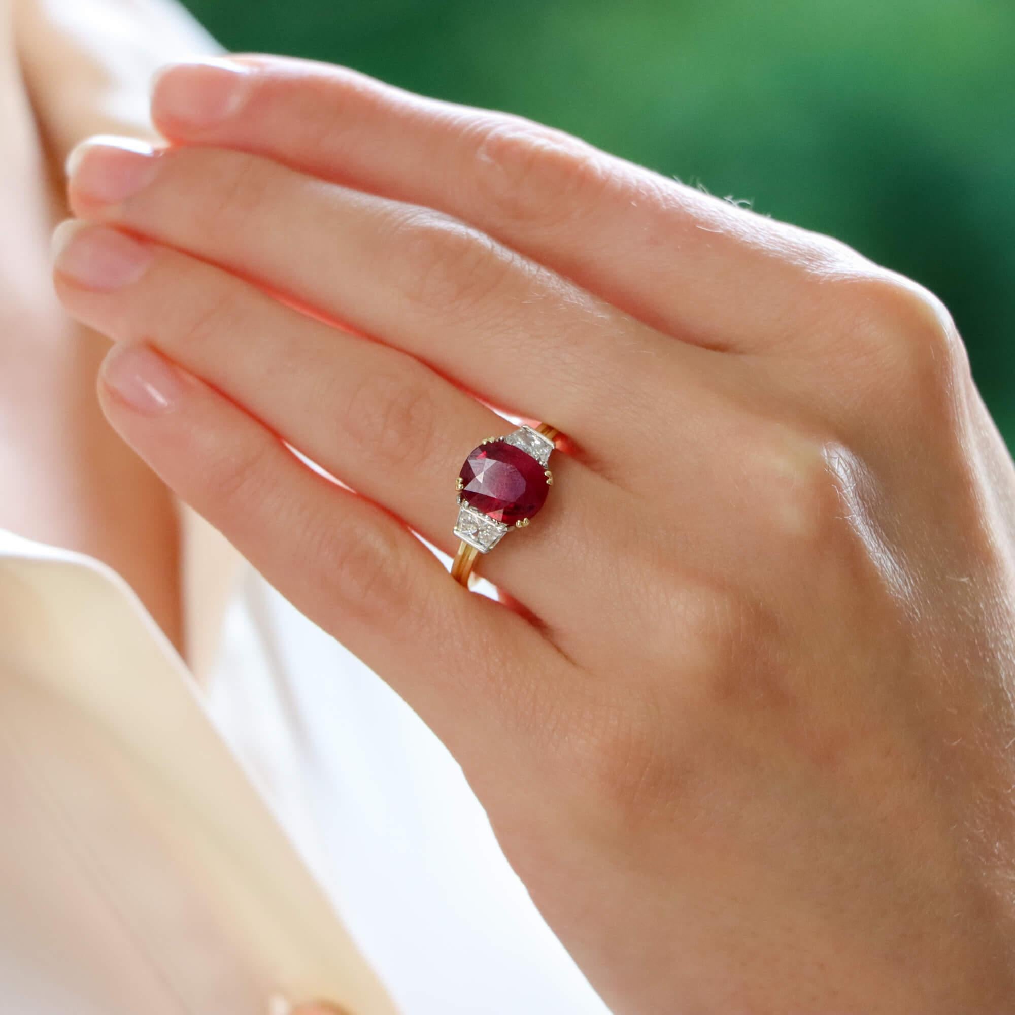 A beautiful ruby and diamond trilogy ring set in 18k yellow gold and platinum.

This classic ring design is centrally set with a astounding certified 3.05 carat oval cut vibrant ruby and is double four claw set in an open back triple setting. The