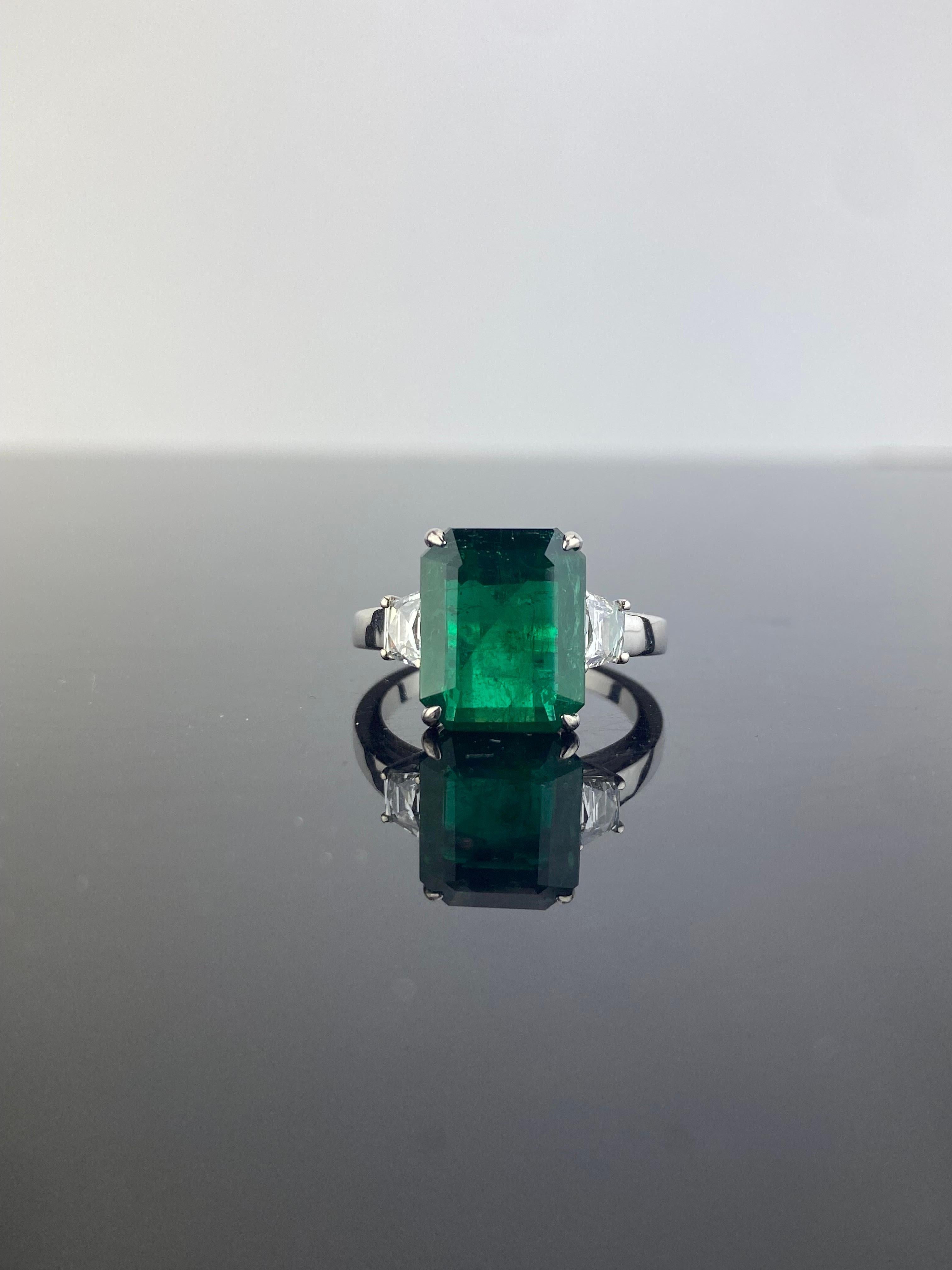 A classic three stone ring, with a 3.90 carat top quality emerald cut Zambian Emerald centre stone and 2 trapeze 0.45 carat side stone White Diamonds. The Emerald is transparent, with an ideal vivid green color and great luster. The ring is