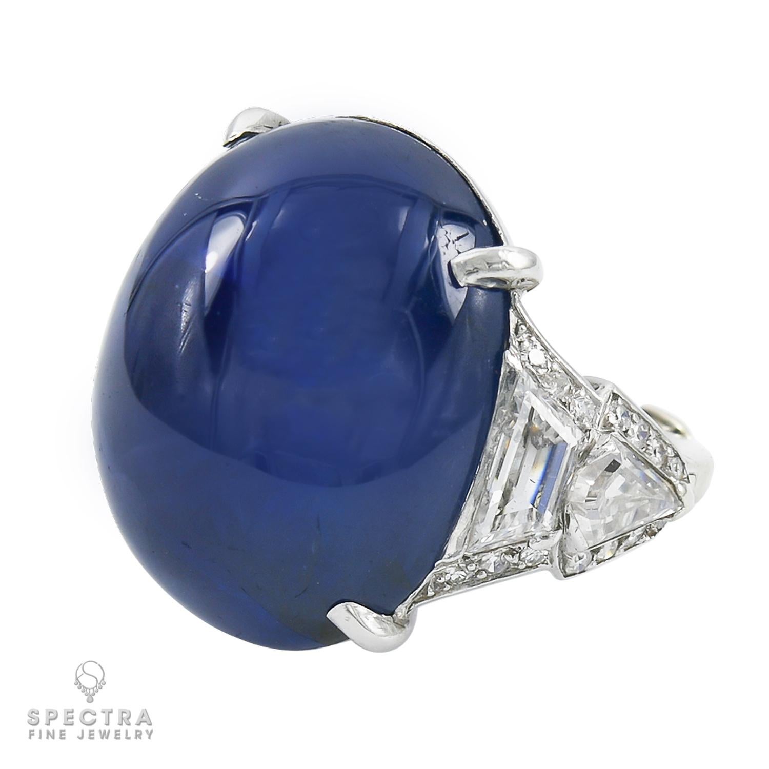 A cocktail ring representing an amazing oval cabochon blue sapphire of Burmese origin with no heat enhancement. Carat weight is 40.59.
Certified by AGL.
The center stone is accented with trapezoid and shield cut diamonds on both sides, approximately