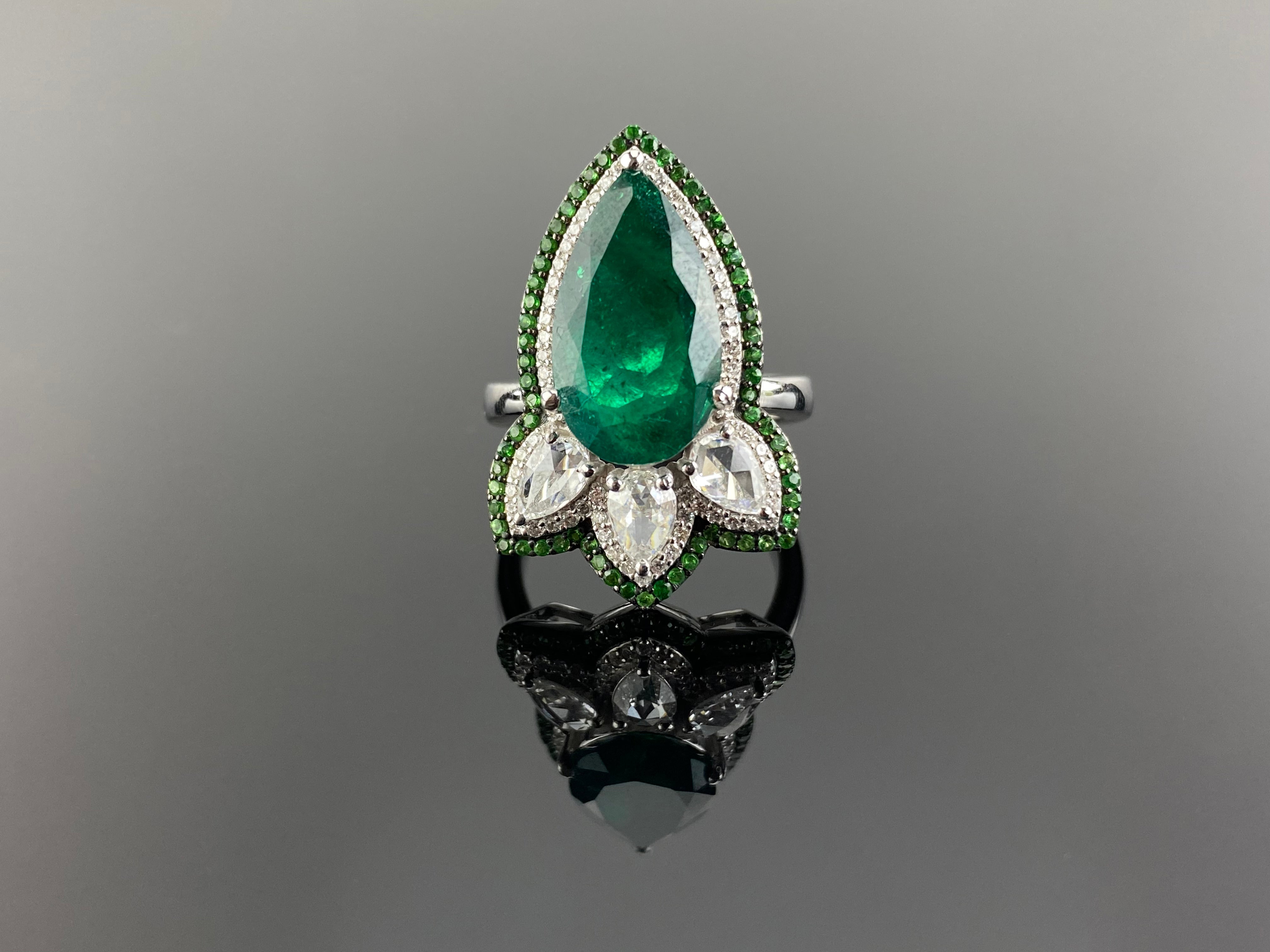 A very uniquely designed certified natural 4.08 carat Zambian Emerald pear shaped, with 0.61 carats of pear shaped White Diamonds, surrounded with Diamonds and Tsavorites - giving it an art-deco look. The center stone is an ideal vivid green color,