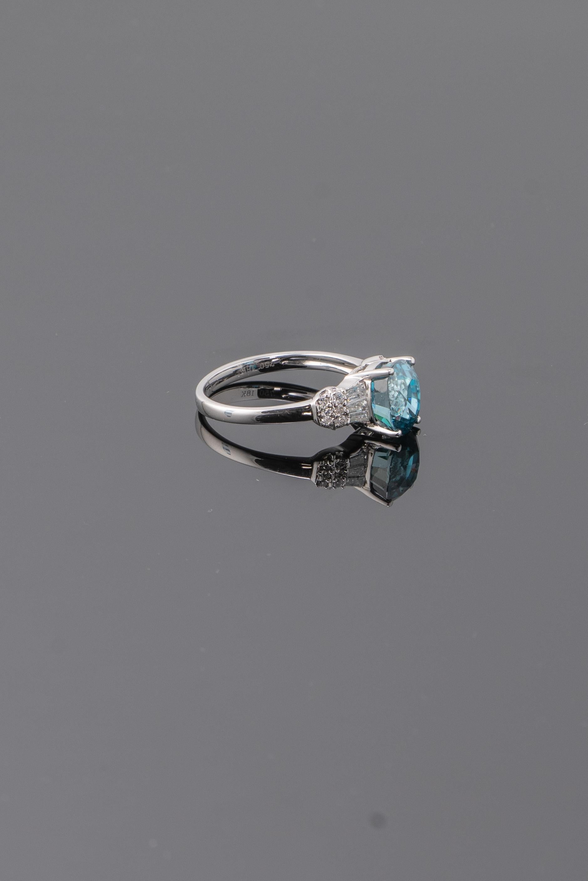 Une pierre naturelle de zircon bleu cambodgien ( Cambodiolite ) pesant 4,28 carats, avec une couleur bleue lumineuse . Les diamants situés à côté de la pierre centrale pèsent 0,41 carats et sont sertis dans 3,14 grammes d'or blanc 18K. La taille de