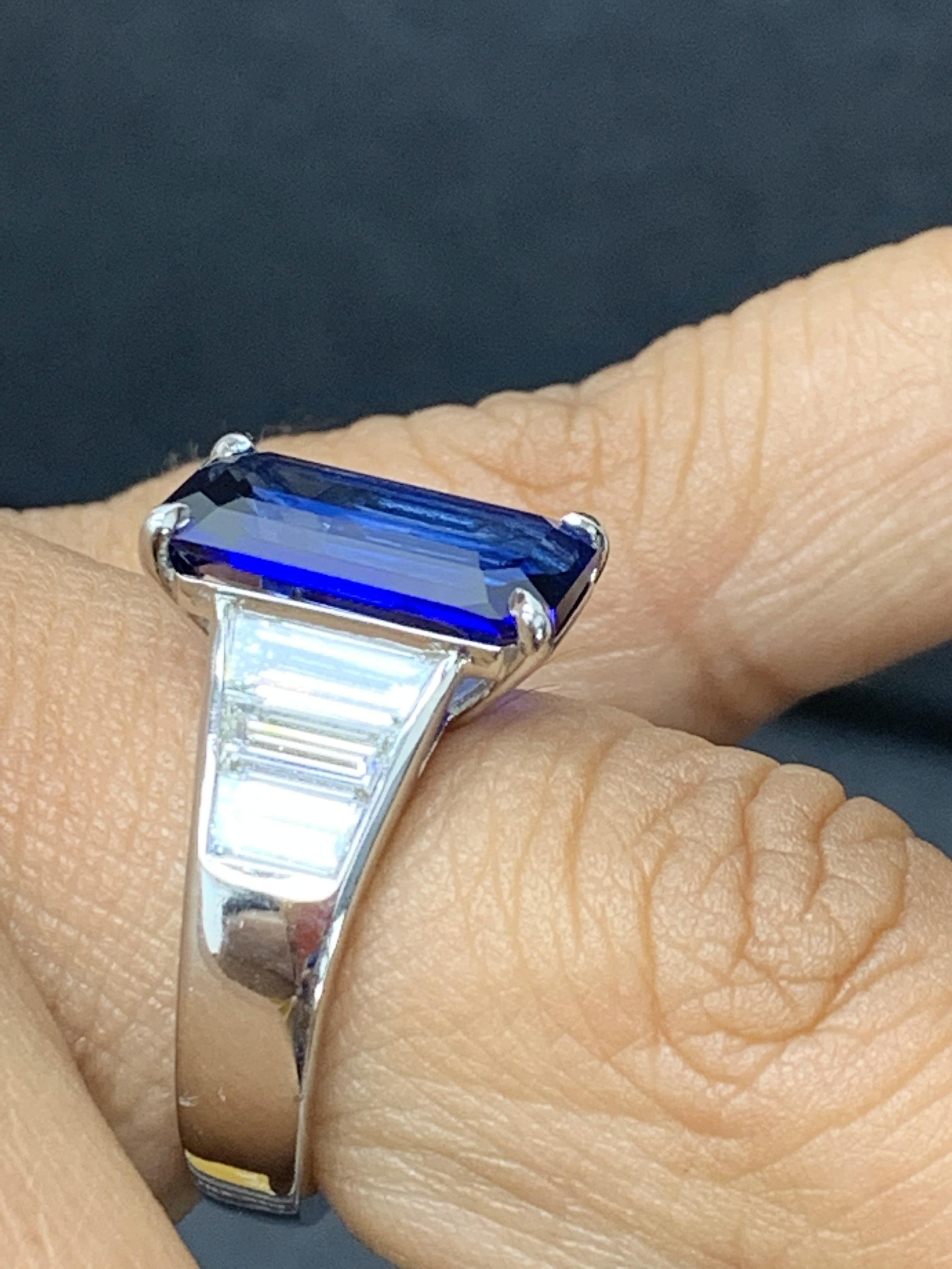 A stunning well-crafted engagement ring showcasing a 5.13-carat certified emerald-cut vivid blue Sapphire. Flanking the center diamond are perfectly matched graduating baguette diamonds, channel set in a polished platinum mounting. 6 Accent diamonds