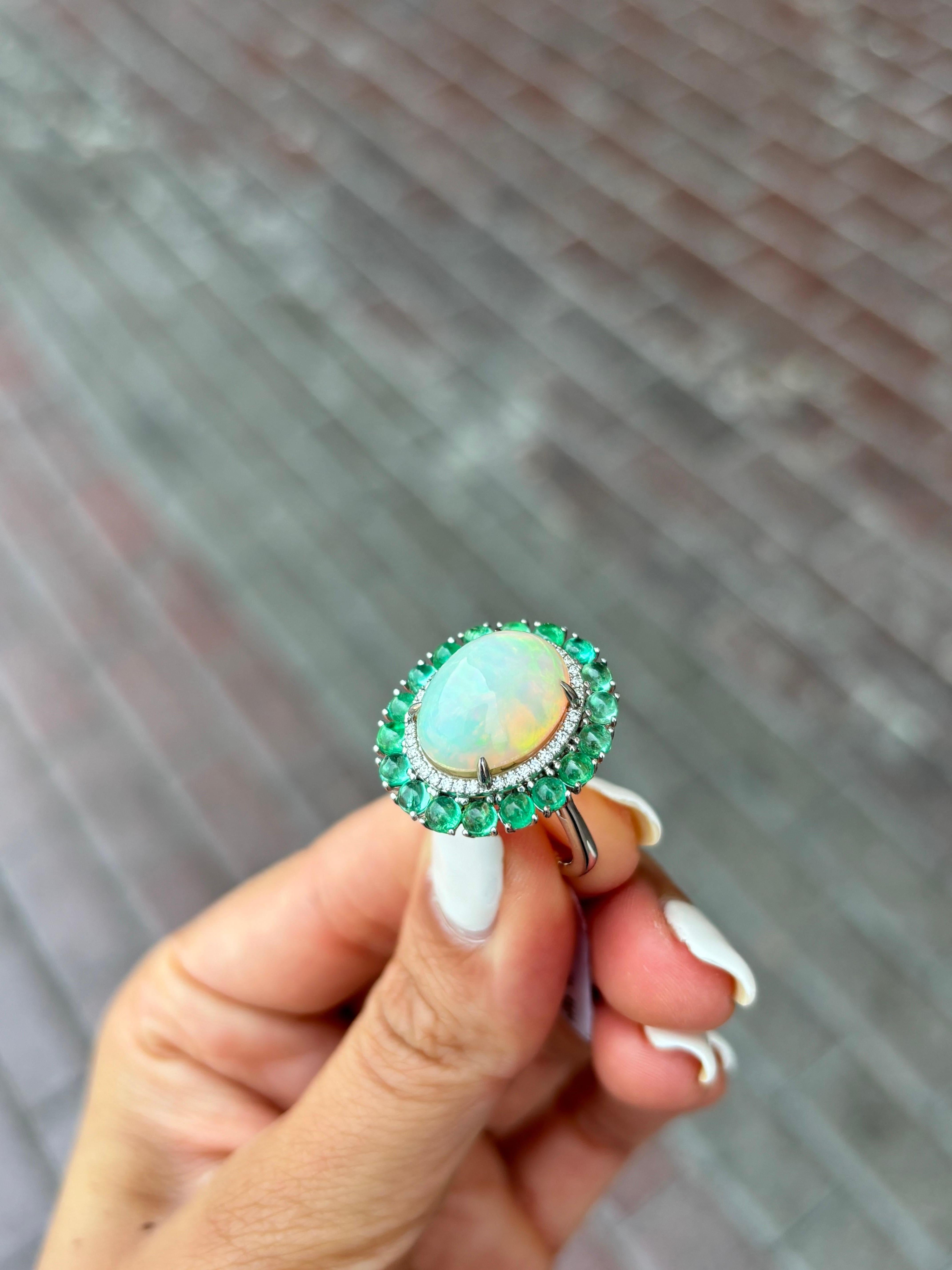 A beautiful combination of 5.64 carat oval shaped Ethiopian Opal cabochon and 2.59 carat Emerald cabochon set in solid 18K White Gold, with 0.23 carat of Diamonds. 
The ring is currently sized at US7, can be resized. 
Certificate available for the