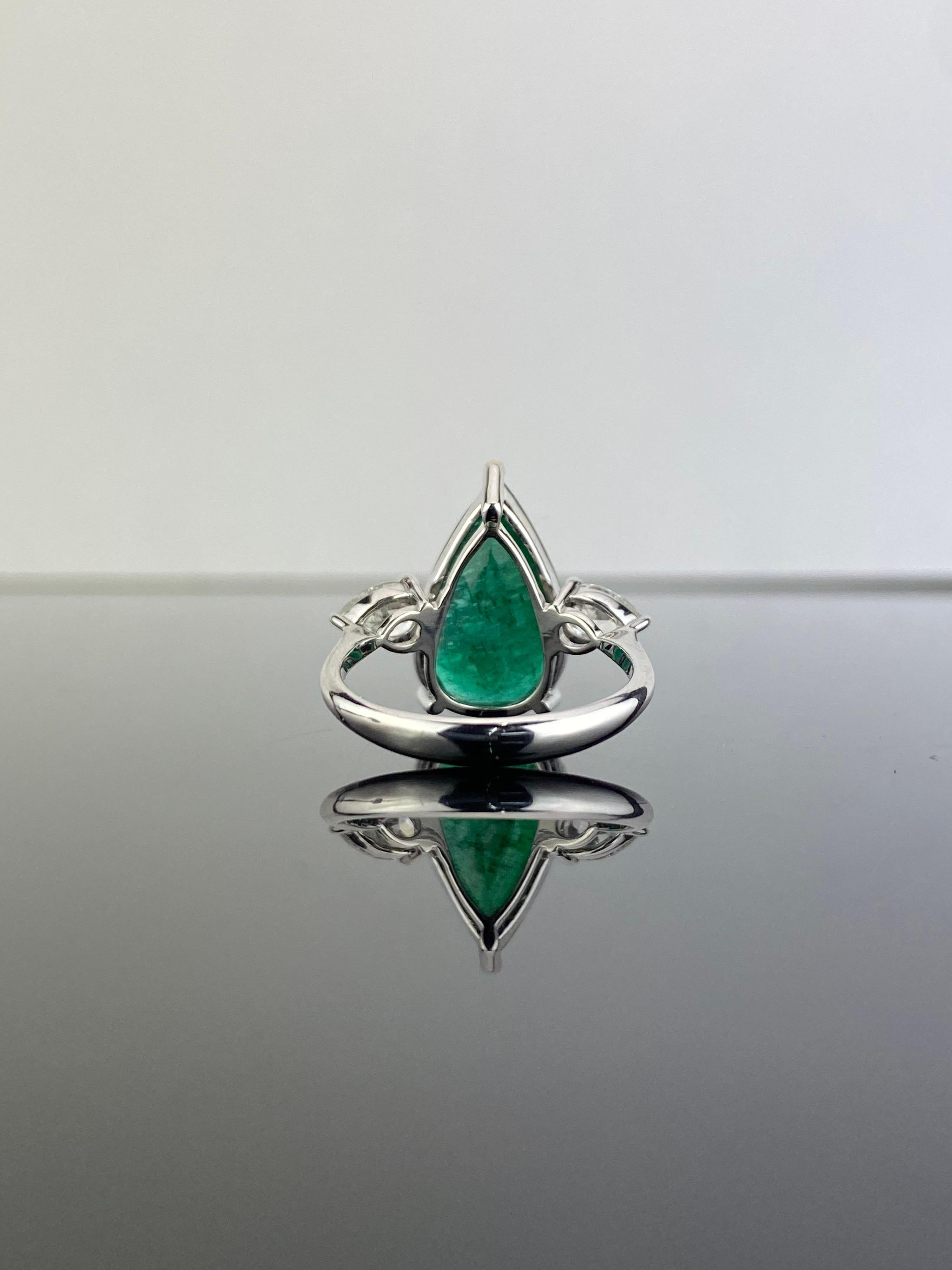 A stunning certified 5.70 carat Emerald and 0.69 carat pear shaped White Diamond three stone, engagement ring. The centre stone is a Zambian Emerald, transparent with a beautiful vivid green color and amazing luster. This ring is set in solid 18K