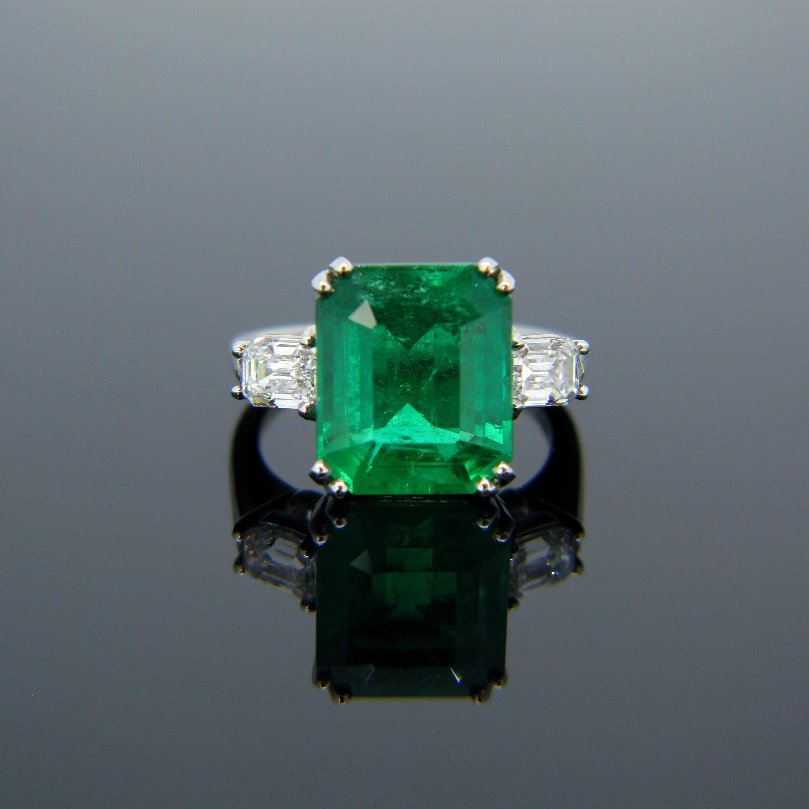 This stunning new ring is made in platinum and features a magnificent 6.05ct Colombian emerald with a vibrant green color. The stone is adorned with two diamonds (one on each side) weighing approximately 0.40ct each. Emerald is also known as the