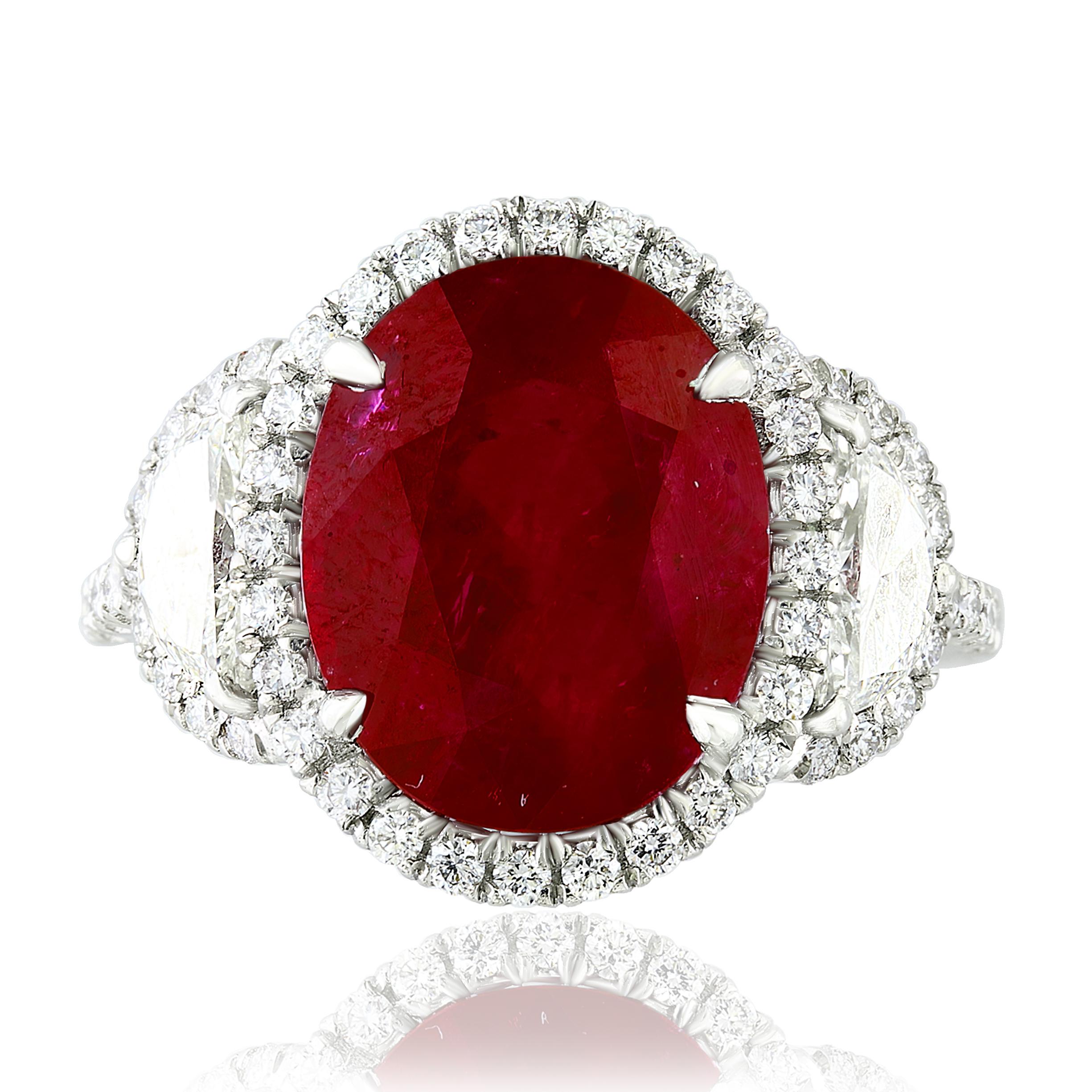 A stunning ring showcasing a rich intense red Oval cut Certified Ruby weighing 6.05 carats surrounded by a row of diamonds. Flanking the center stone are two brilliant cut half-moon diamonds, weighing 0.59 carats total, framed in a brilliant diamond