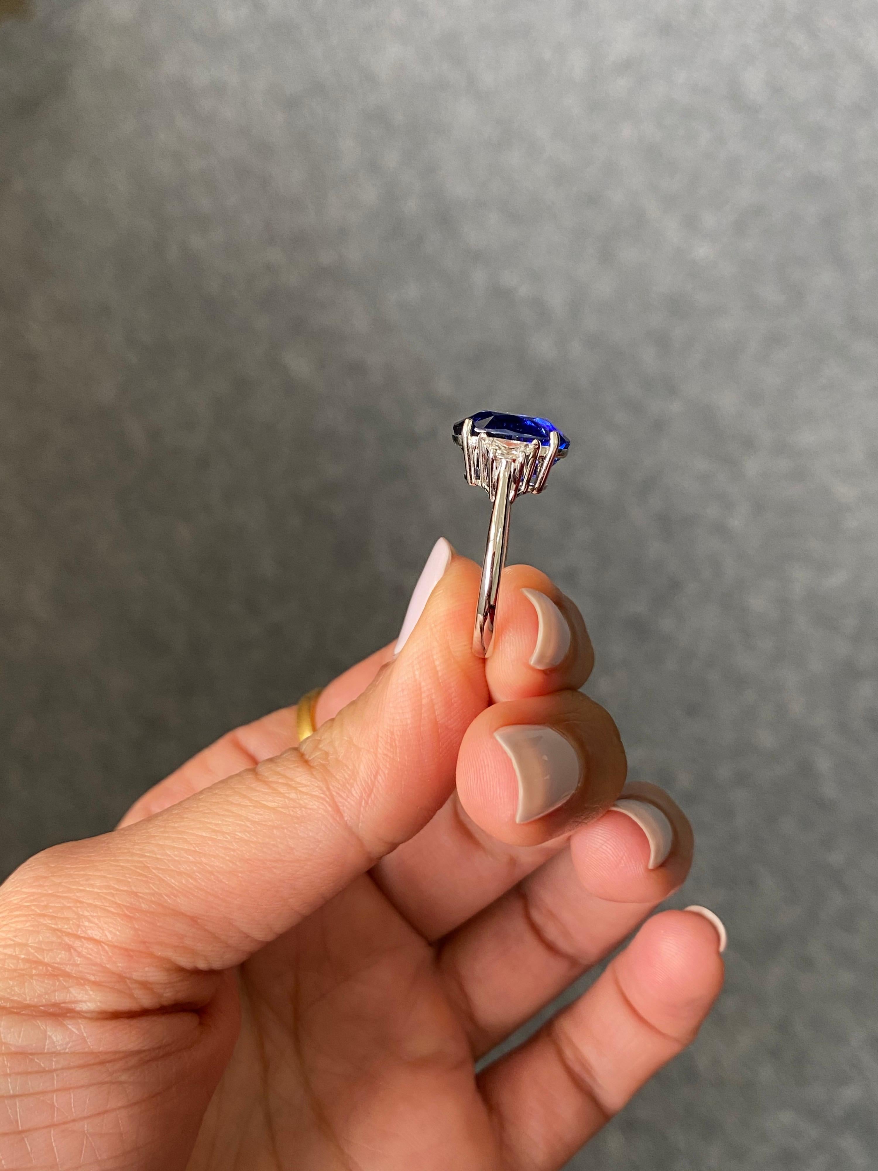Une bague de fiançailles classique à trois pierres, avec un saphir bleu de Ceylan (Sri Lanka) de forme ovale de 6,53 carats et des diamants trapèze incolores de qualité VS de 0,36 carat. La pierre centrale n'a pas d'inclusions, elle est très