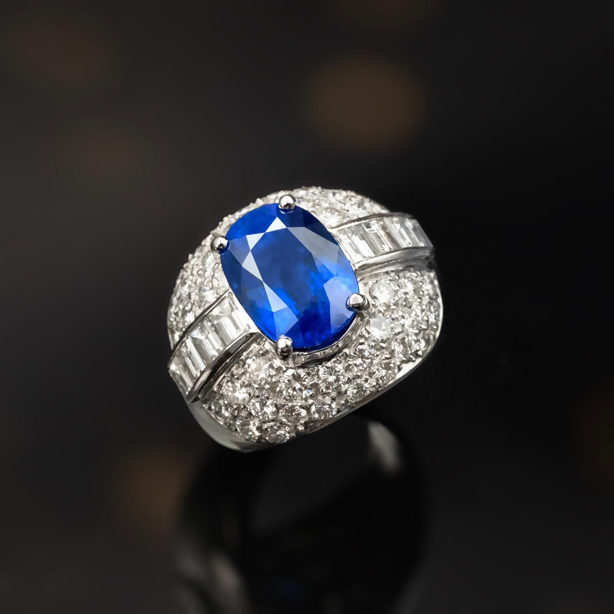 This exquisite dome ring features a magnificent central sapphire, weighing 6.85 carats boasting a Vivid and highly sought-after Royal Blue hue, as certified.  
The sapphire is complemented by a line of baguette-cut diamonds on each side and