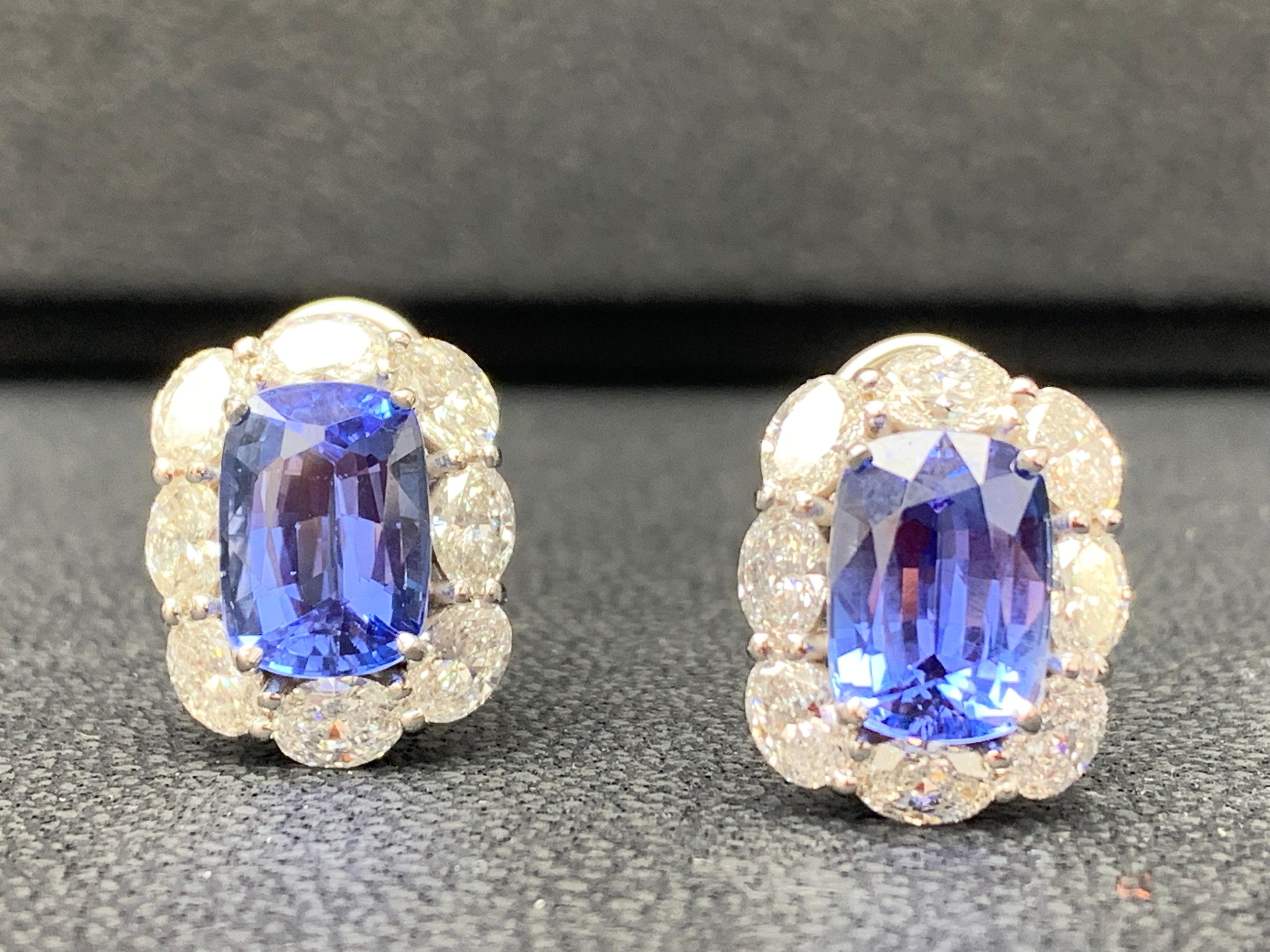 Showcasing two color-rich Certified Cushion cut Vivid Blue Sapphires weighing 8.49 carats total, surrounded by a single row of oval cut brilliant diamonds. 16 Accent diamonds weigh 3.19 carats total. Set in 18 karats white gold. Omega Clip with the