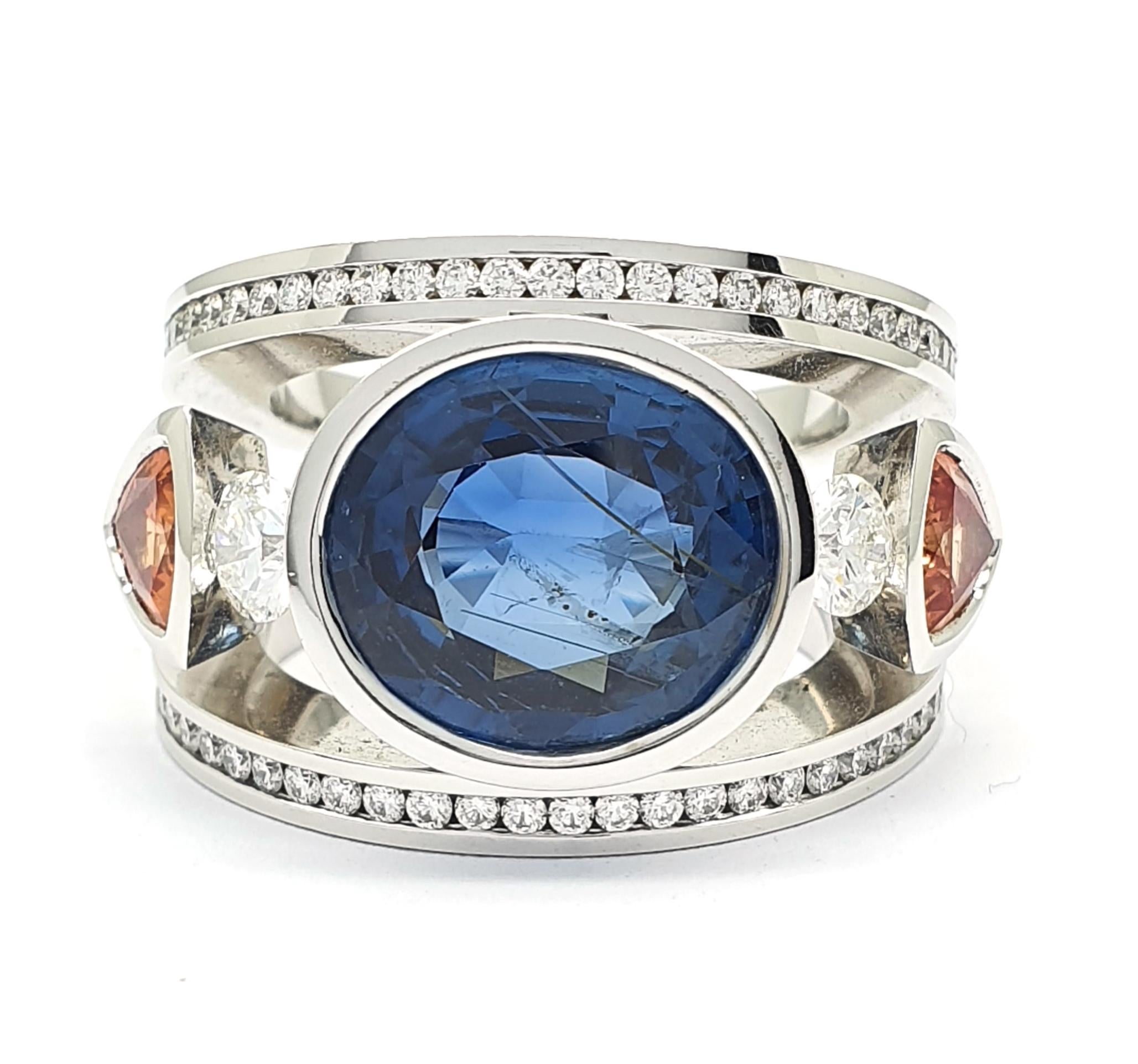 This ring is a unique piece that was handcrafted in Eigenmann's own studio in The Hague.  It is an 18Krt white gold retro ring with 2 triljant sharpened orange corundums and oval sharpened Sri Lanka Sapphire of 9.45c.  The sapphire is a natural