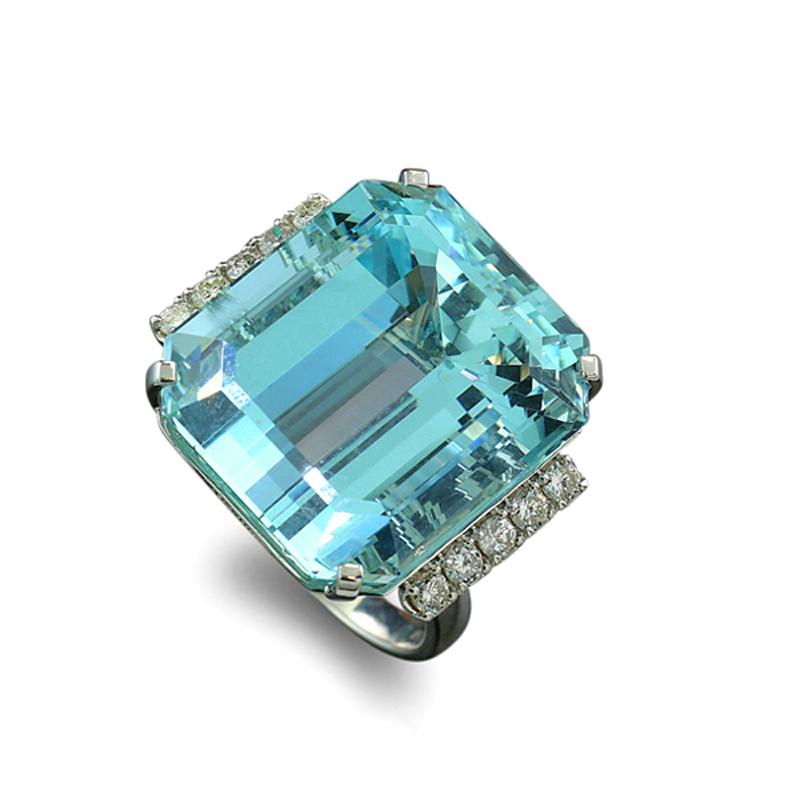 espectacular anillo con una aguamarina de 27,82 quilates, en talla esmeralda. La gema tiene una claridad nítida y un brillo radiante, y está engastada en un bisel lineal con dos garras. La exquisita aguamarina azul está enmarcada por 10 diamantes