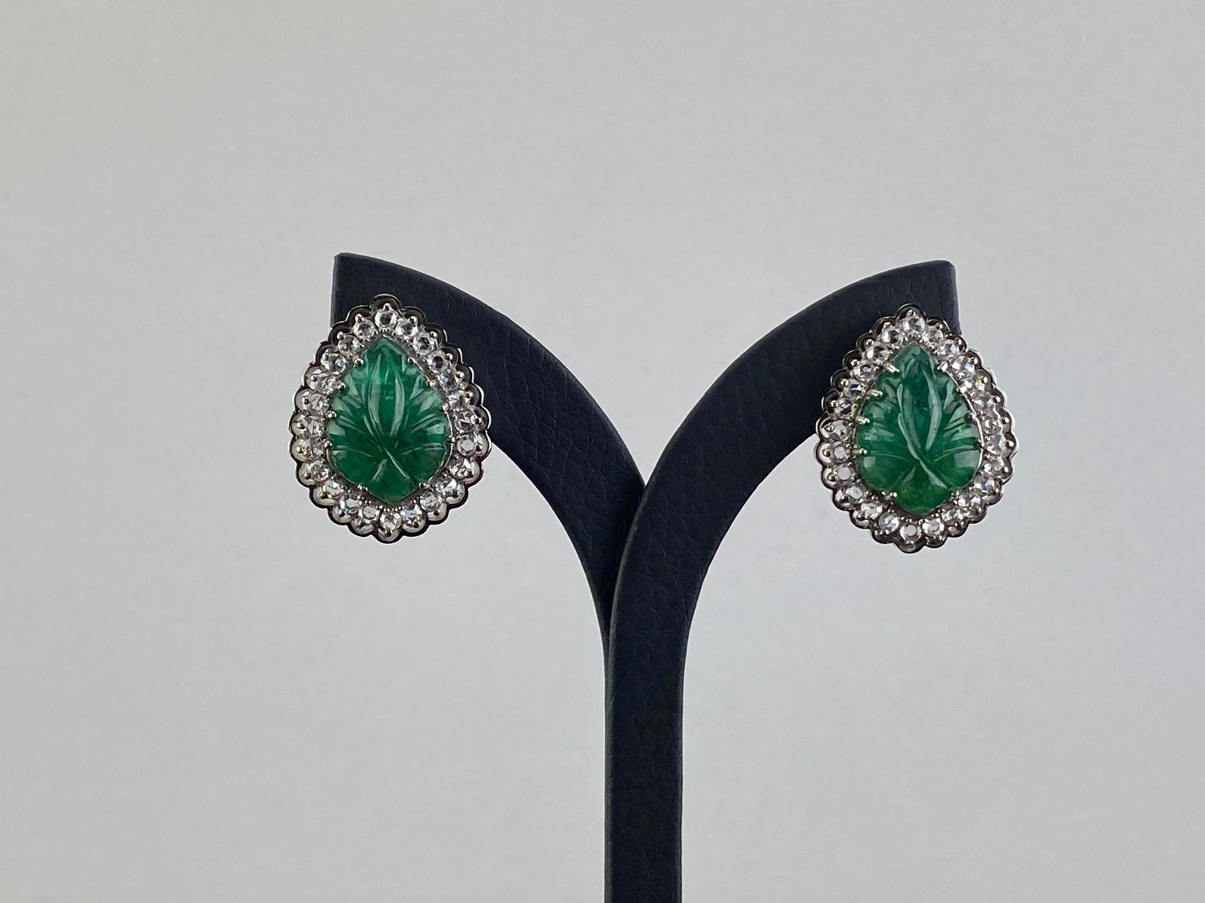 These fabulous stud earrings feature emeralds carved of Zambian weighing 19.04 Carats . The carving is exceptionally well cut in the pink city of Jaipur . There are inclusions in all four gems, typical of the material. The emeralds are complimented