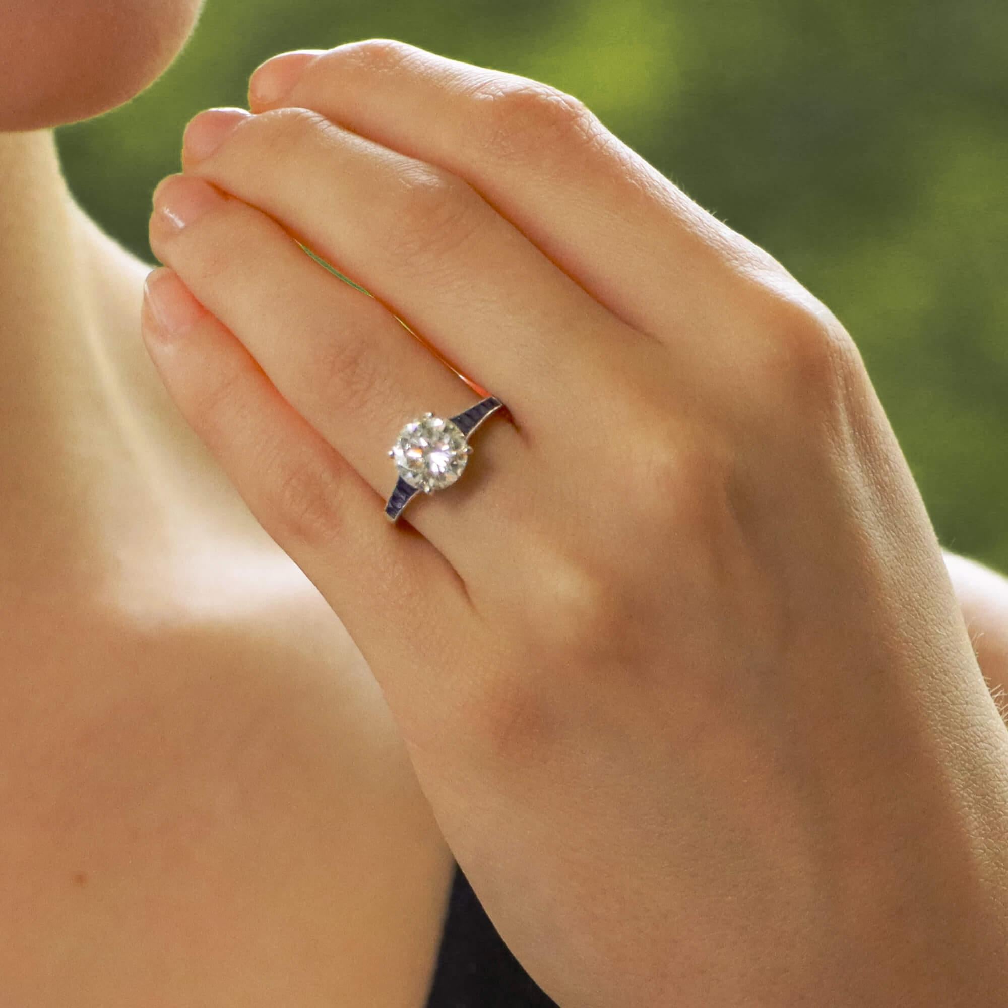 Ein wirklich schöner, vom Art Deco inspirierter Verlobungsring mit Diamanten und Saphiren, gefasst in Platin.

Der Ring ist mit einem funkelnden zertifizierten runden Diamanten im Brillantschliff besetzt, der mit vier Krallen in die Mitte gesetzt