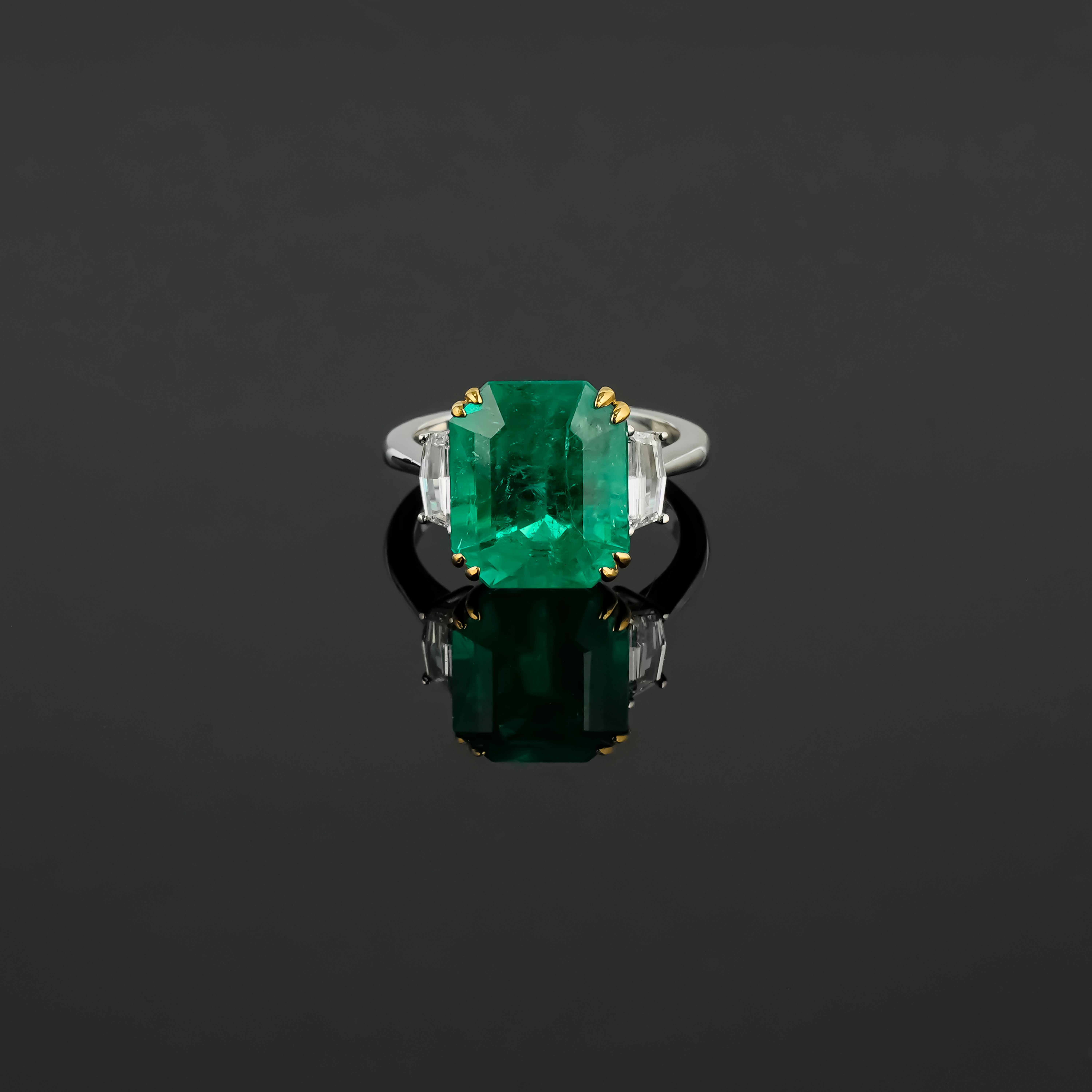 Magnificent Colombian Emerald: This ring features an exceptional 7.14-carat octagonal Colombian emerald, renowned for its vibrant, deep green color and unparalleled clarity, making it a highly prized gemstone.

Flanked by two cadillac-cut diamonds