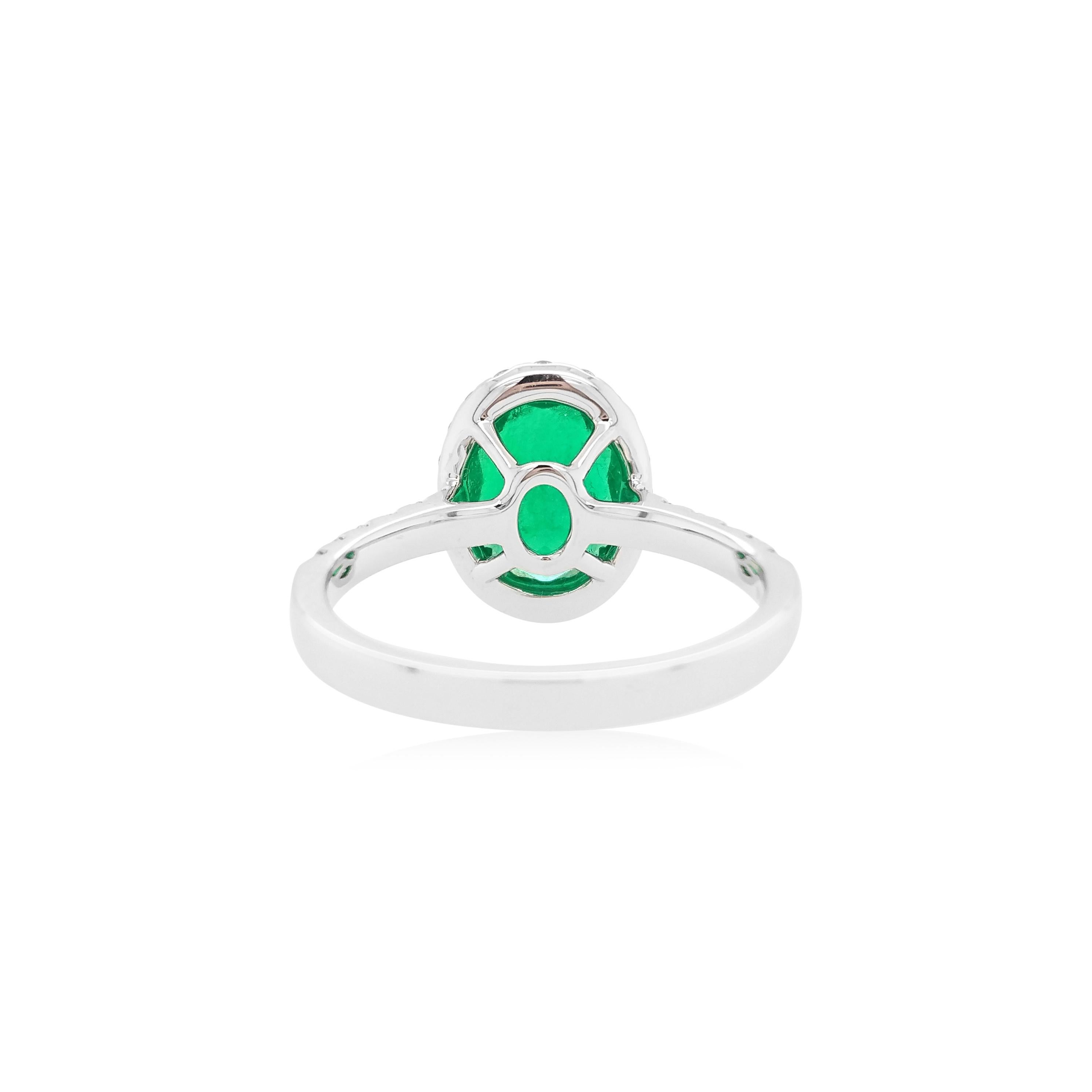 Dieser elegante Ring zeigt einen glänzenden ovalen kolumbianischen Smaragd in der Mitte, der von einem zarten weißen Diamanten umgeben ist. Dieser Ring ist in 18 Karat Weißgold gefasst, um die spektakulären Farbtöne des Smaragds und das Funkeln der