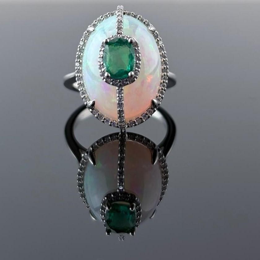 This ring features a 10.13 carat natural white Opal with a color-play effect. It is set on a 18K white gold band and accented with natural G, VS diamonds weighing 0.42 carats. In the center of the ring , there is a emerald supported by a diamond