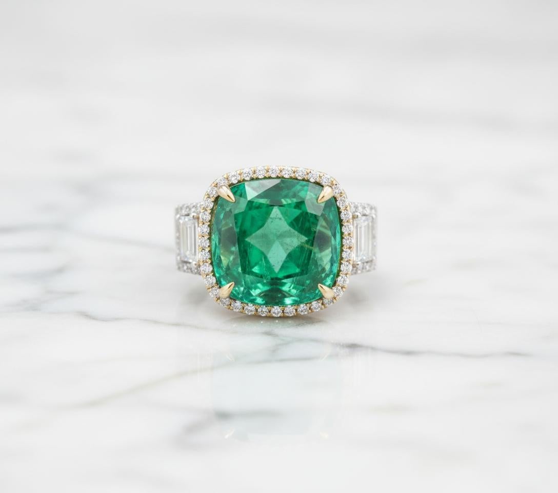 Este espectacular anillo contemporáneo exhibe una esmeralda casi natural de talla cojín de un rico y vibrante color verde. Engarzada en una cálida cesta de oro amarillo, la esmeralda está bellamente enmarcada por un brillante halo de diamantes, que