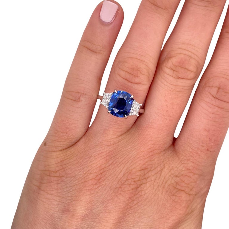 Ring contains one cushion cut sapphire 4.22ct and 2 side trapezoid diamonds, 0.72tcw. Diamonds are F in color and VS2 in clarity.  Stones are mounted in a handmade basket prong setting in 18k white gold. Top of ring, including all three stones,