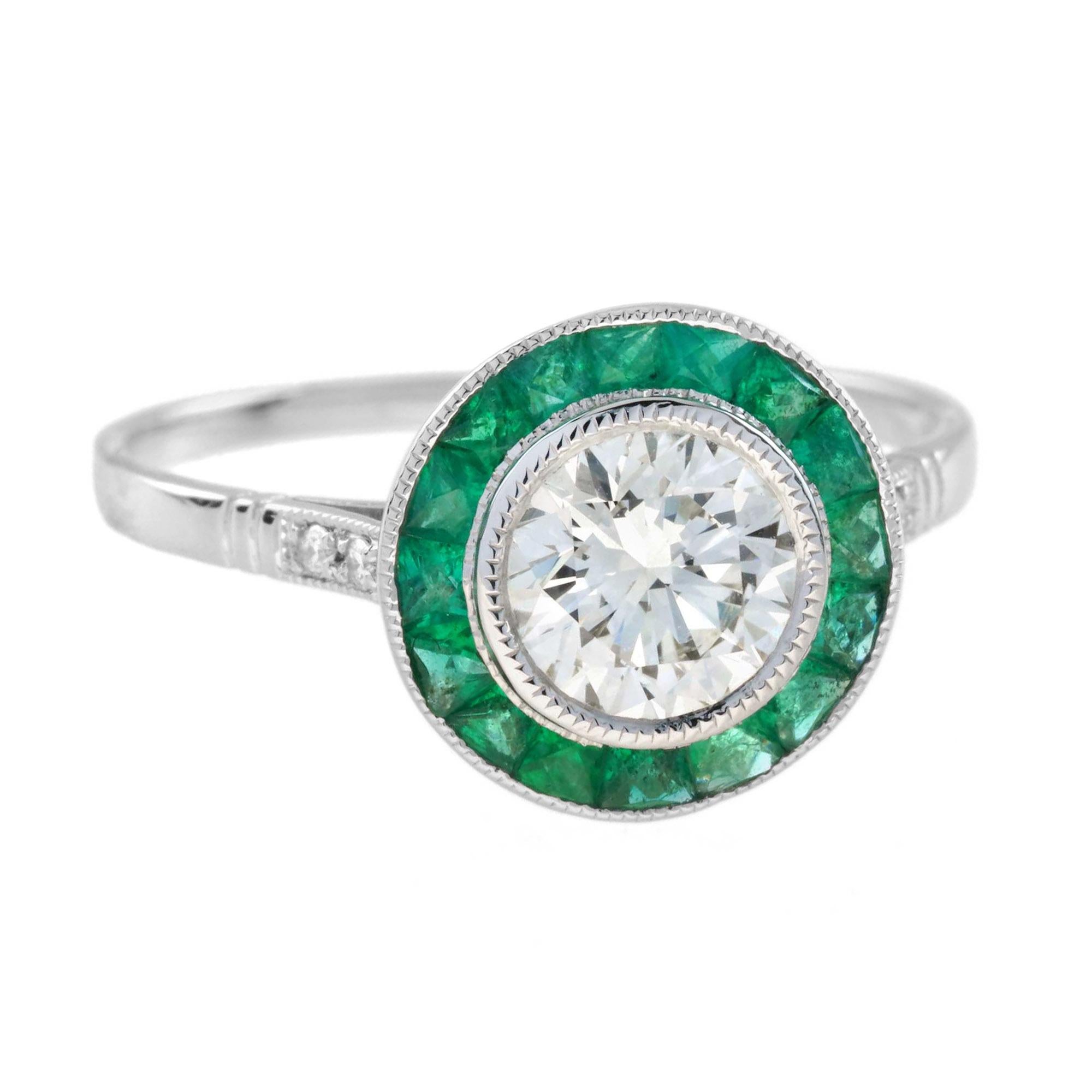 Ein vom Art Deco inspirierter Zielring mit einem zentralen, von GIA zertifizierten 1-Karat-Diamanten in der Lünette mit einer Farbe von N und einer Reinheit von VVS1. Der zentrale Diamant ist von einem Halo aus kanalgefassten Smaragden im
