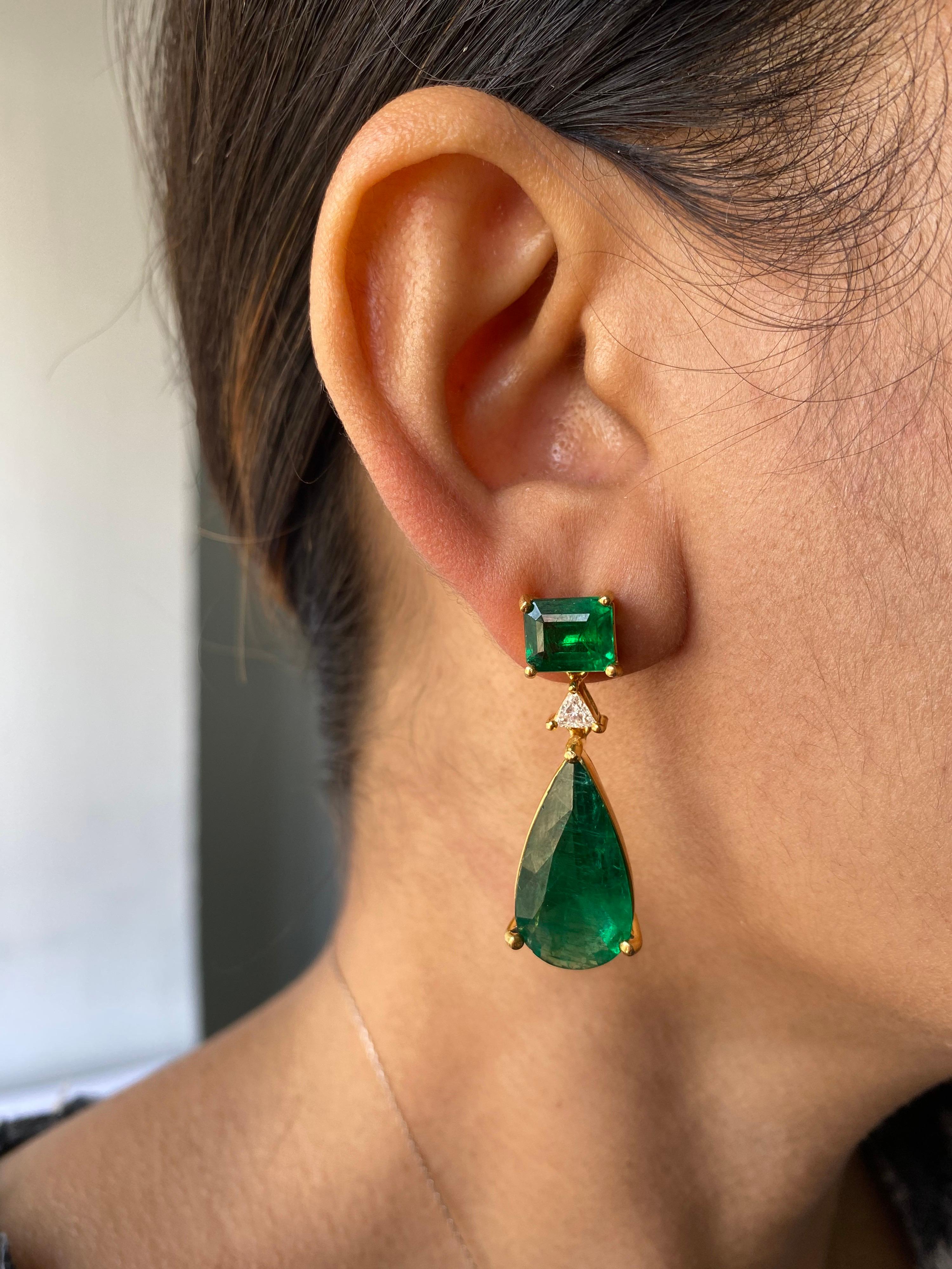 A classic and very elegant pair of Zambian Emerald earrings, with trillion shaped Diamond connecting the Emerald cut and Pear shape Emeralds, all set in solid 18K Yellow Gold. The Zambian Emeralds are transparent, with an ideal vivid green color and