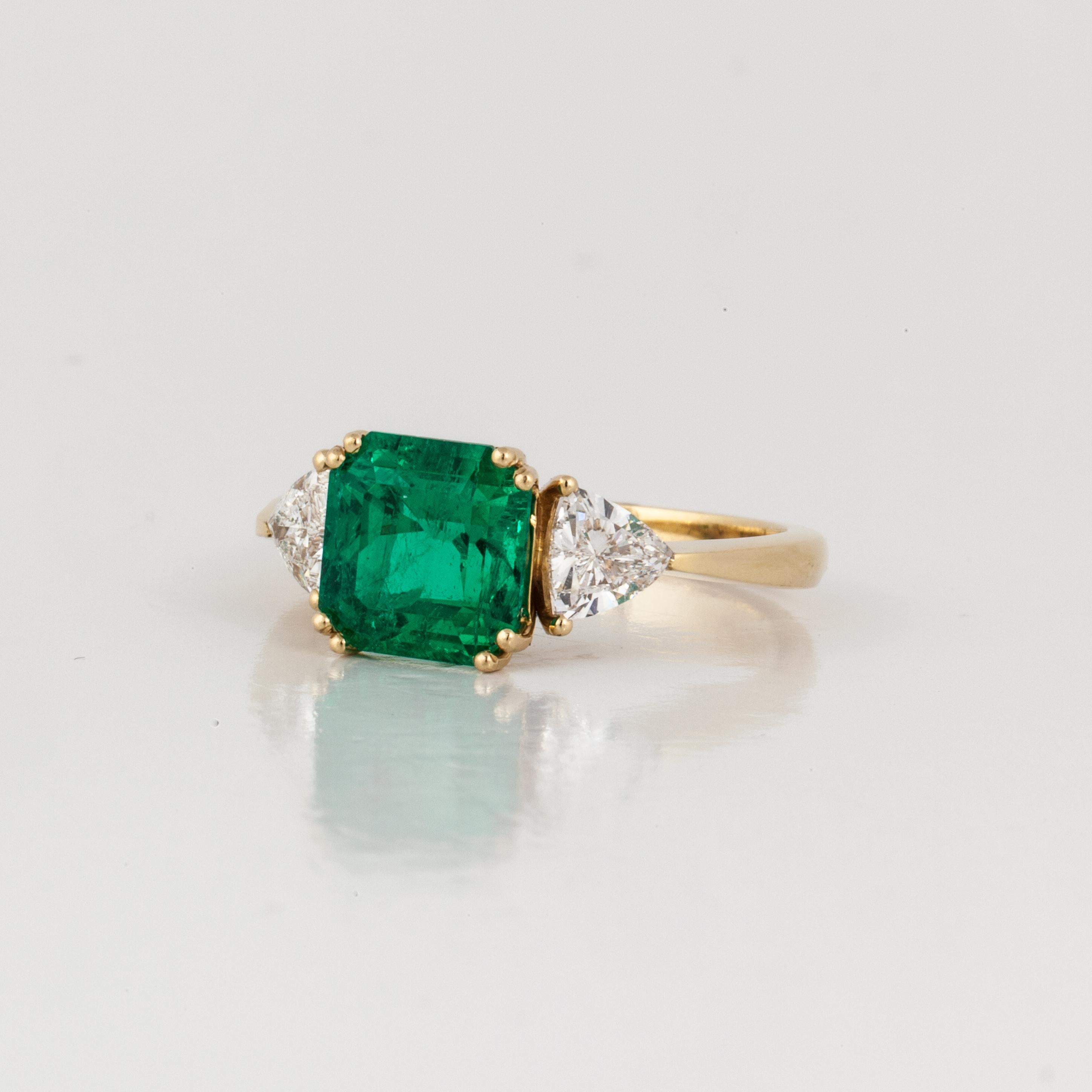 18K yellow gold ring featuring an AGL certified emerald accented with diamonds. The 2.30 carat emerald-cut emerald is accompanied by an AGL report stating, Columbian/minor.  Additionally, there are 2 triangular-cut diamonds that total 0.80 carats;