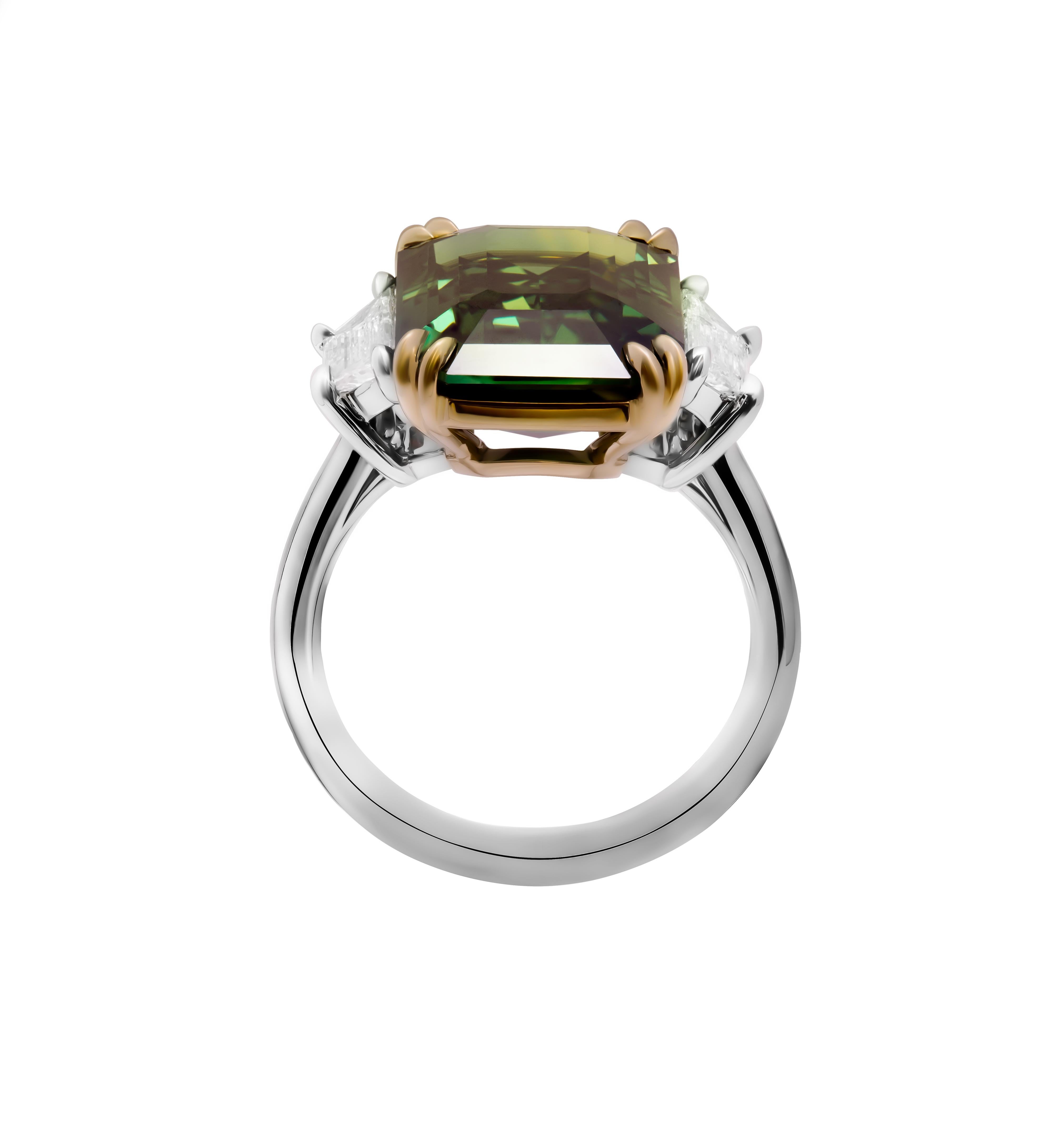 Elegance and sophistication converge in this breathtaking three-stone ring, a timeless masterpiece crafted in the luxurious combination of 18k yellow gold and 950 platinum. At its heart sits a magnificent 10.07 carat emerald-cut green sapphire,