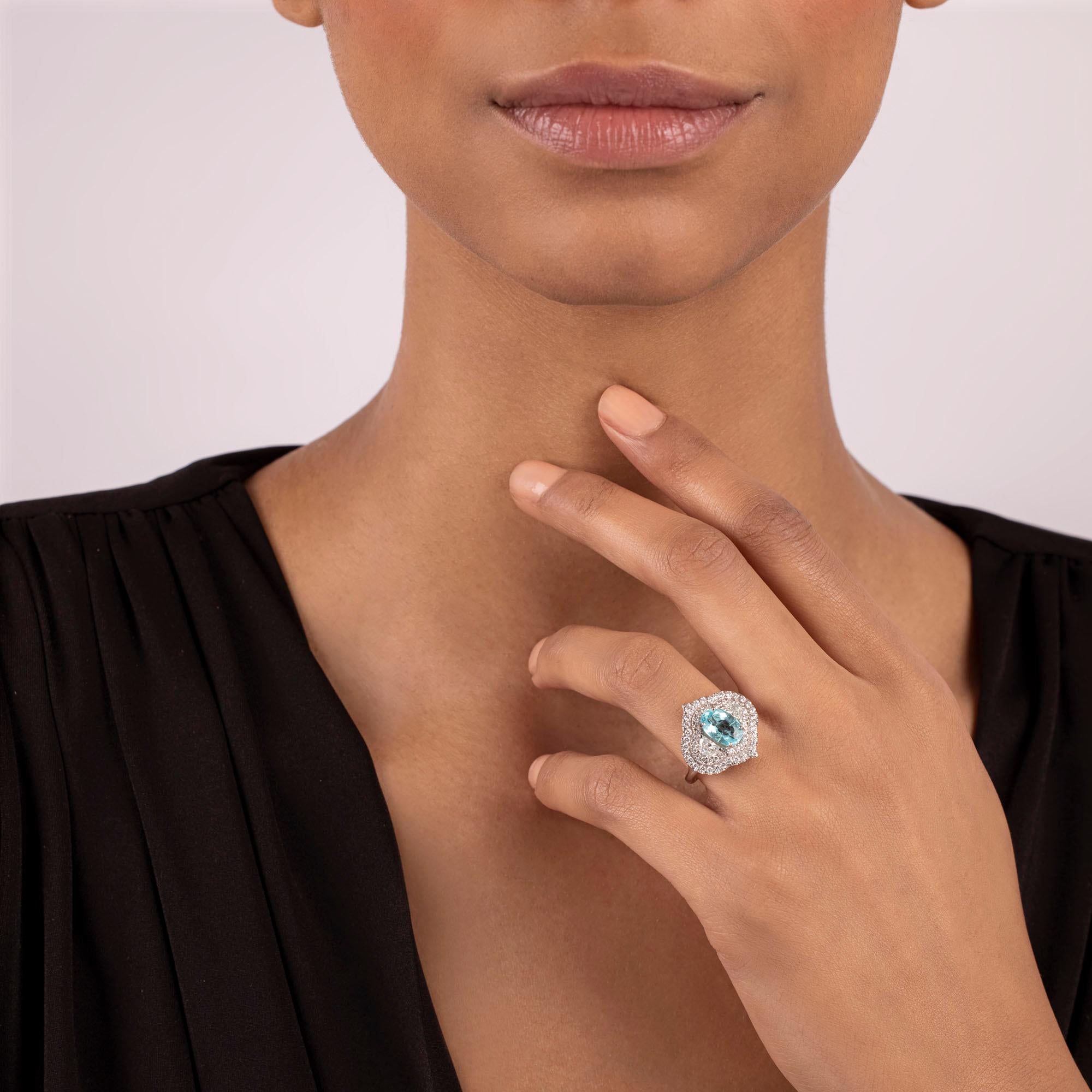 A luminous Paraiba is nestled between two shimmering half moon diamonds and set within the confines of a double halo design. Petite diamond pointers outline the center composition adding an unmatched brilliance that sparkles with each motion. A