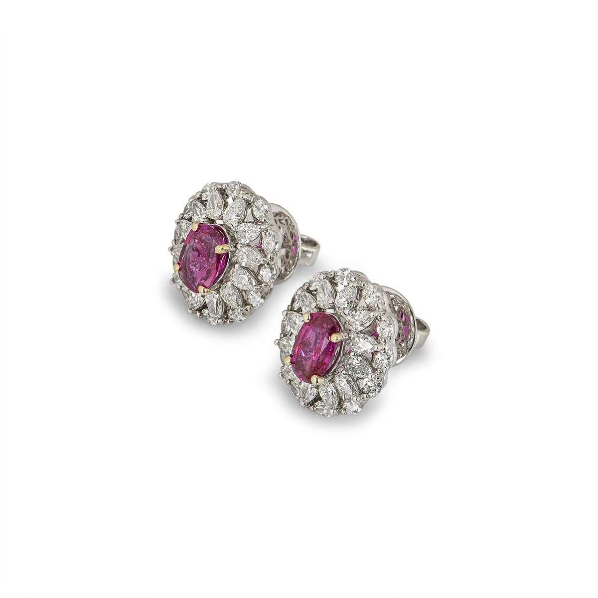 A pair of 18k white gold ruby and diamond earrings. The earrings are set with 2 oval cut pinkish-red natural Burmese rubies, weighing 1.38ct and 1.53ct. Surrounding the rubies are pear cut and marquise cut diamonds, totalling 2.75ct. The earrings