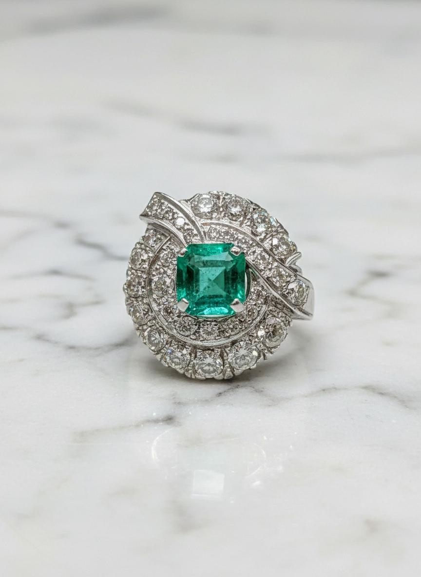 Dieser wunderschöne Ring besteht aus einem natürlichen grünen Smaragd, der in 14 Karat Weißgold gefasst ist und von funkelnden Diamanten akzentuiert wird, die seine lebhafte Farbe und seinen klassischen Charme unterstreichen. Der Smaragd ist in