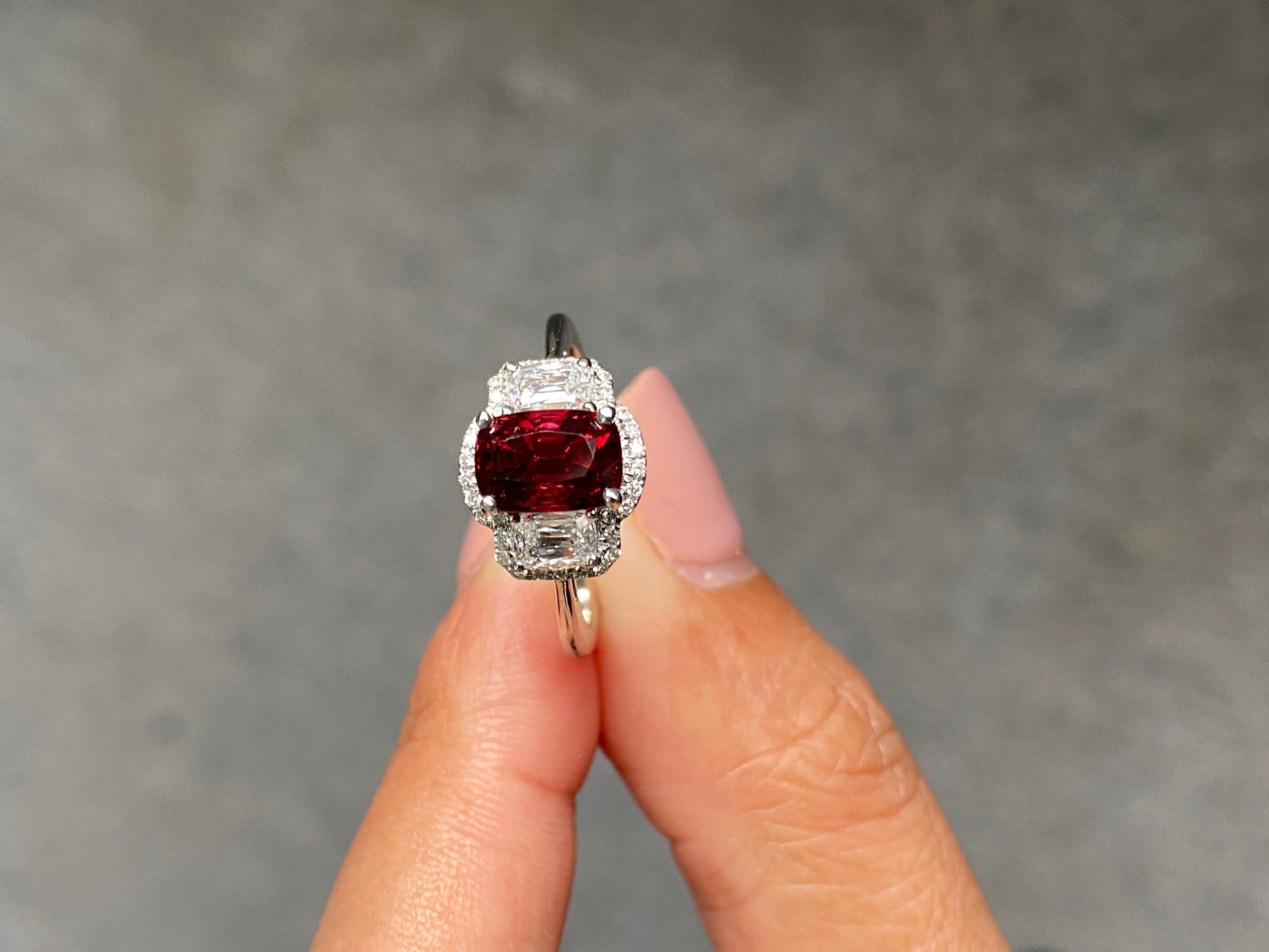 This ring is crafted in 18K white gold, features a rare, vivid red natural spinel from Myanmar as its centerpiece, measuring 7.5 x 5 mm and weighing 1.88 carats. Flanked by 2 large sparkling diamonds totaling 0.47 carats, this design brings together